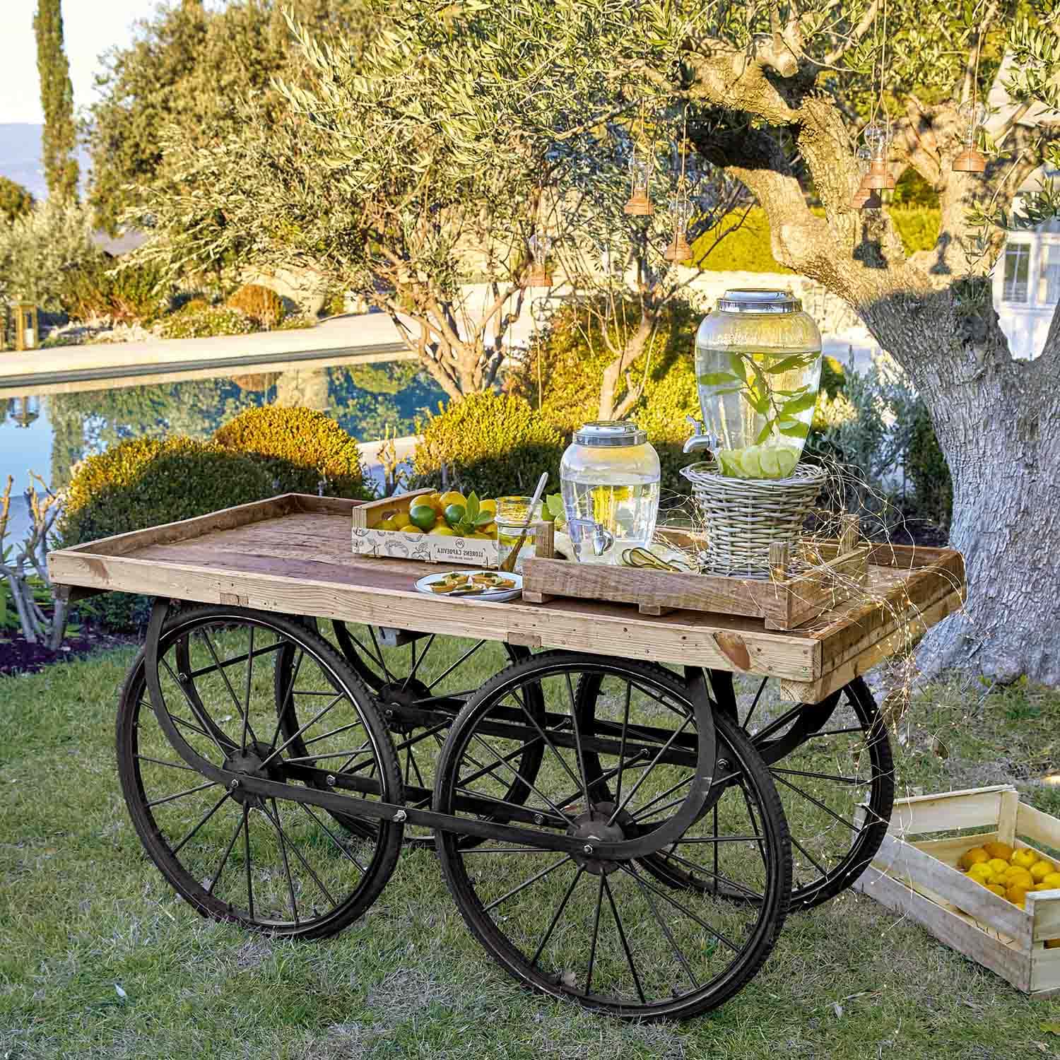 Holzwagen mit schwarzen Rädern und Glaswasserbehältern mit Zitrone im Garten