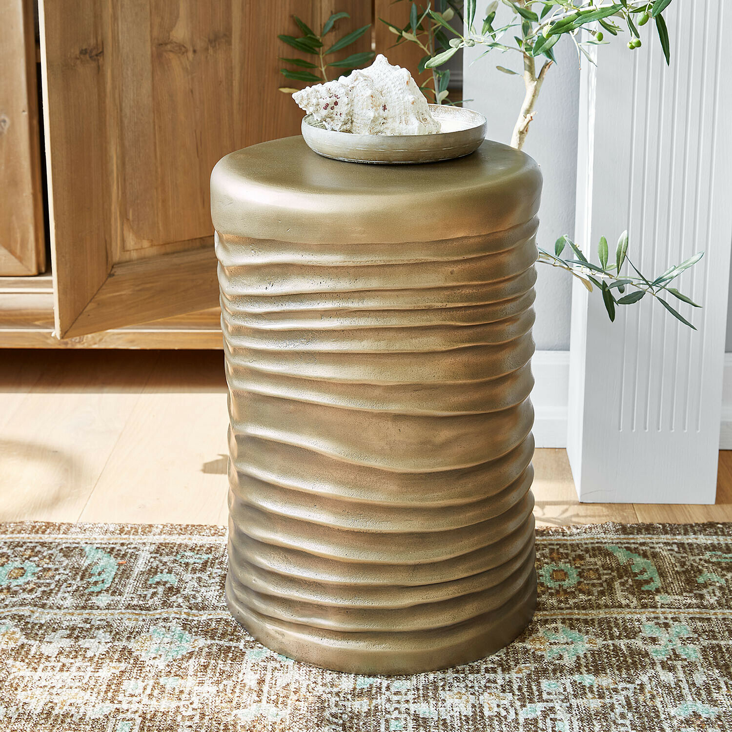 Goldener Metall-Beistelltisch mit welliger Struktur auf Teppich in hellem Raum