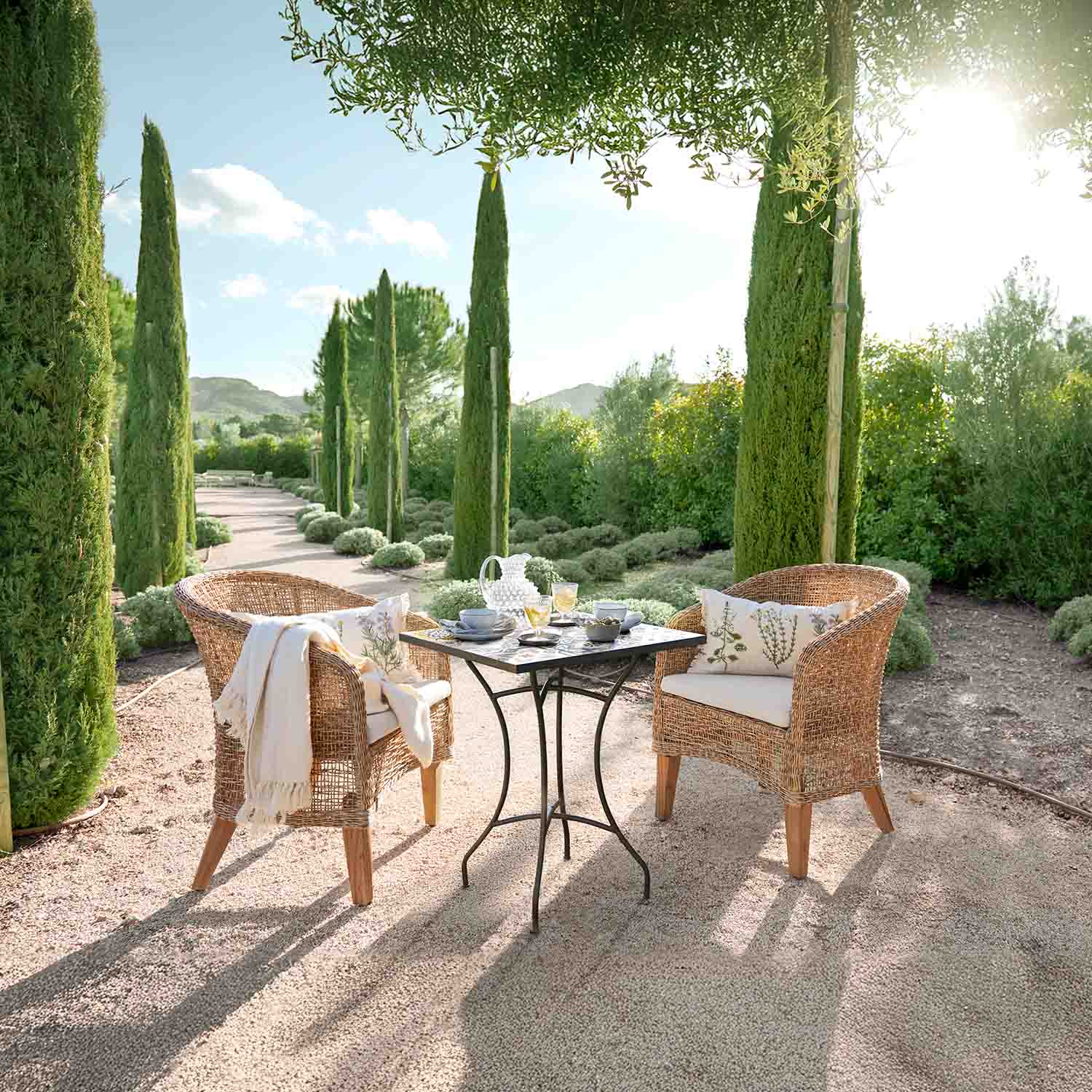 Gartenmöbel-Set aus Rattan mit Kissen und Metalltisch auf sonniger Terrasse im Garten