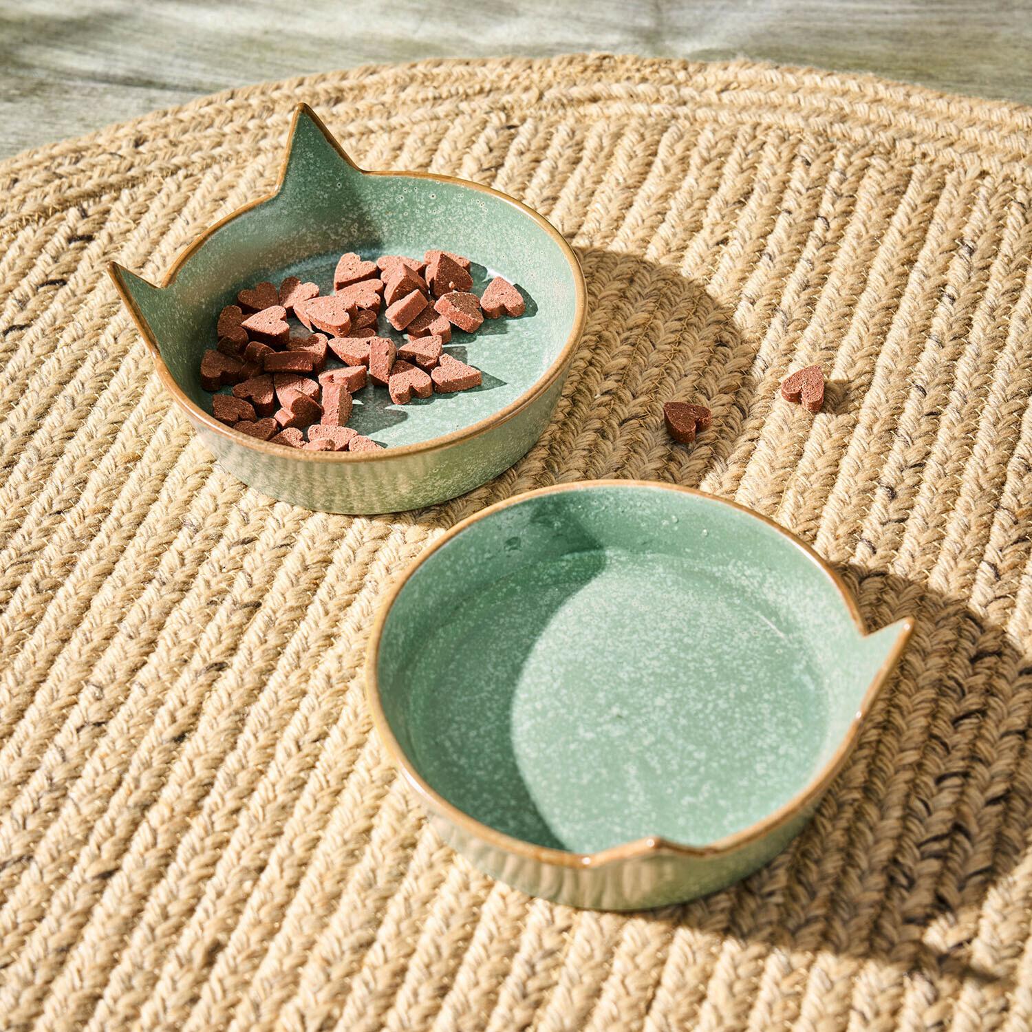 Grüne Keramikschale mit Katzenohren auf geflochtenem Teppich, Schale mit herzförmigem Katzenfutter