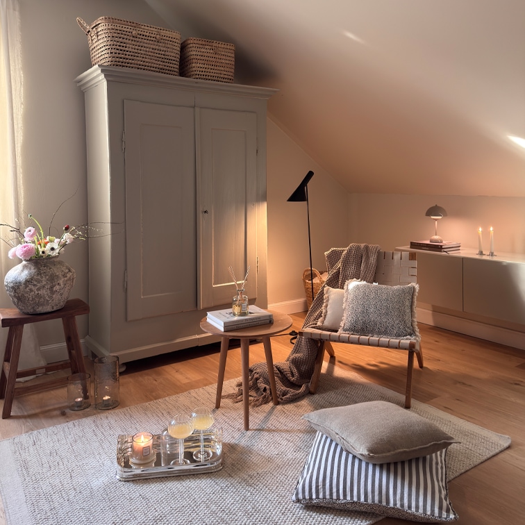 Gemütliches Wohnzimmer mit beigem Sessel, Holztisch und Schrank unter der Dachschräge, Dekorationen und Lampen