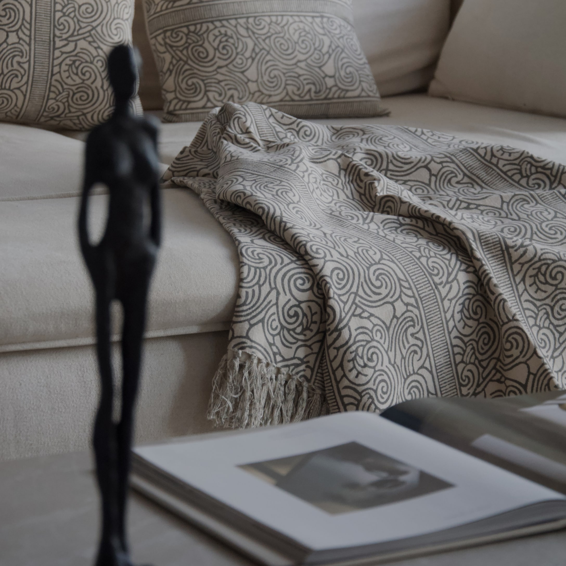 Beige Decke mit grauem Muster und Fransen auf hellem Sofa mit dekorativen Kissen