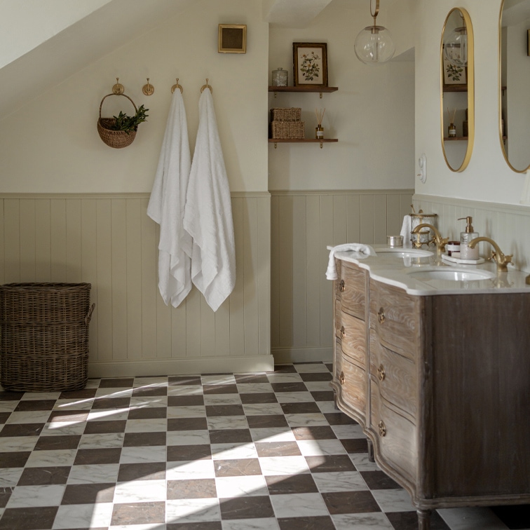 Badezimmer mit kariertem Marmorboden, Holzkommode und weissen Handtüchern an Haken