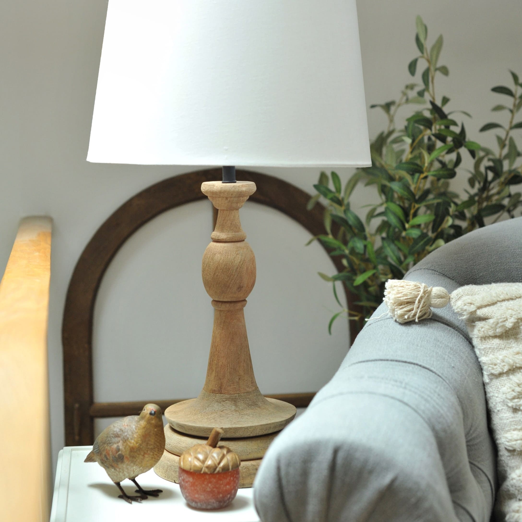 Tischlampe mit Holzfuss und weissem Lampenschirm auf Beistelltisch neben grauem Sofa und Dekoration