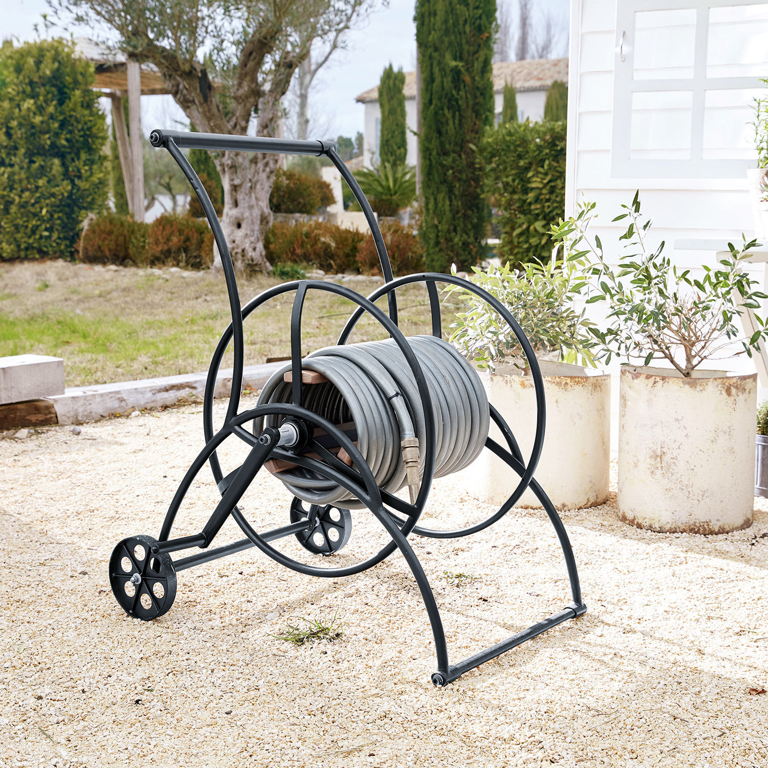 Schlauchwagen Middleby Schwarzer Metallwagen mit grauem Gartenschlauch auf Kiesfläche im Garten