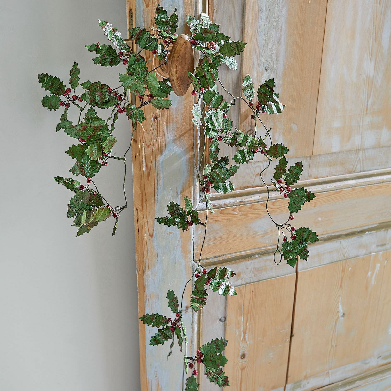 Dekorativer Kranz mit grünen Blättern und roten Beeren an Holztür, festliche Weihnachtsdekoration