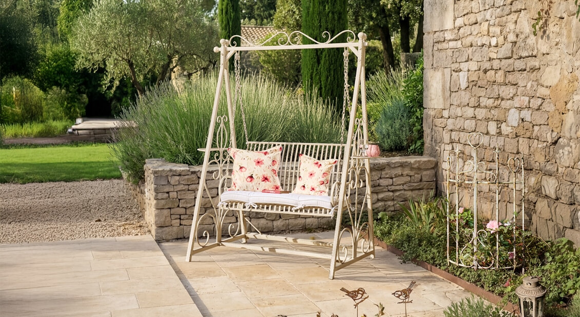Weisse Metall-Gartenschaukel mit rot-weissen Blumenmustern auf Kissen auf Stein-Terrasse