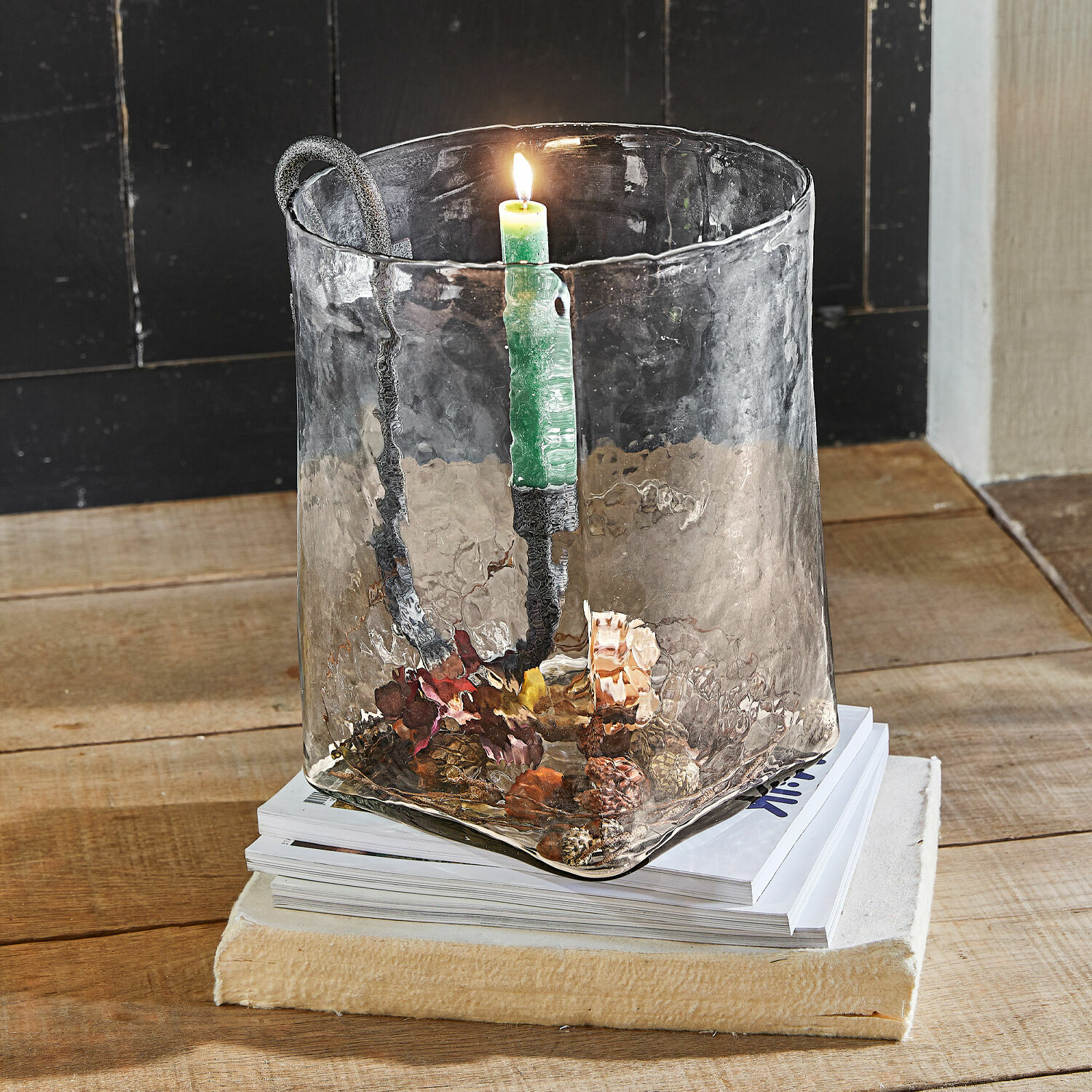 Windlicht Arcene Glas-Kerzenhalter mit Metallgriff und grüner Kerze auf Holztisch mit Zapfendekoration