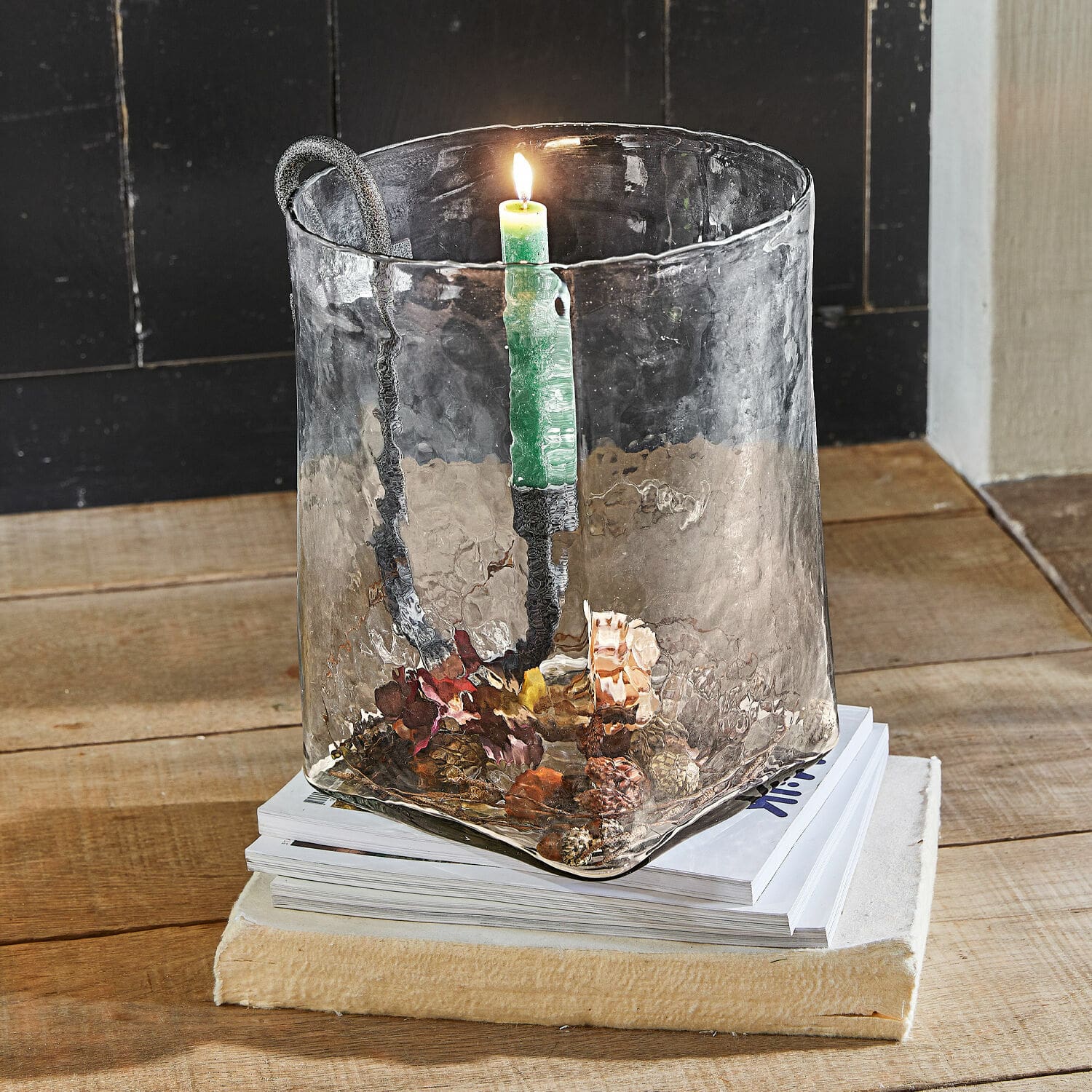 Windlicht Arcene Glas-Kerzenhalter mit Metallgriff und grüner Kerze auf Holztisch mit Zapfendekoration