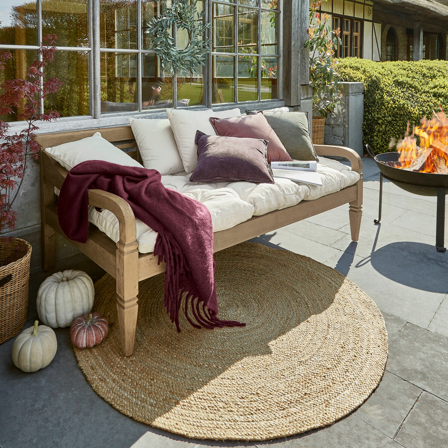 Bank Fairwood Holzbank mit cremefarbenen Kissen und bordeauxroter Decke auf Terrasse mit Juteteppich