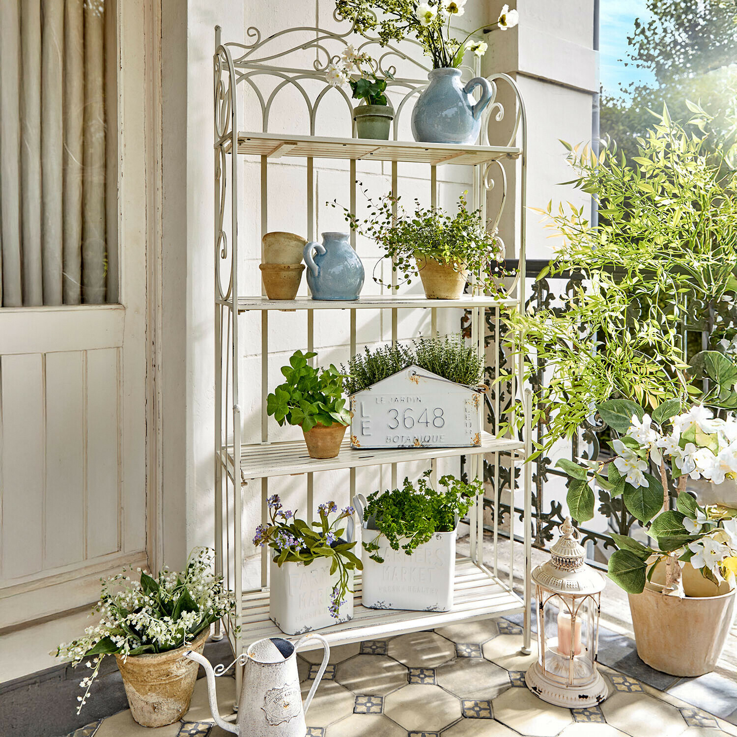 Weisses Metallregal mit Topfpflanzen und Dekorationen auf hellem Balkon