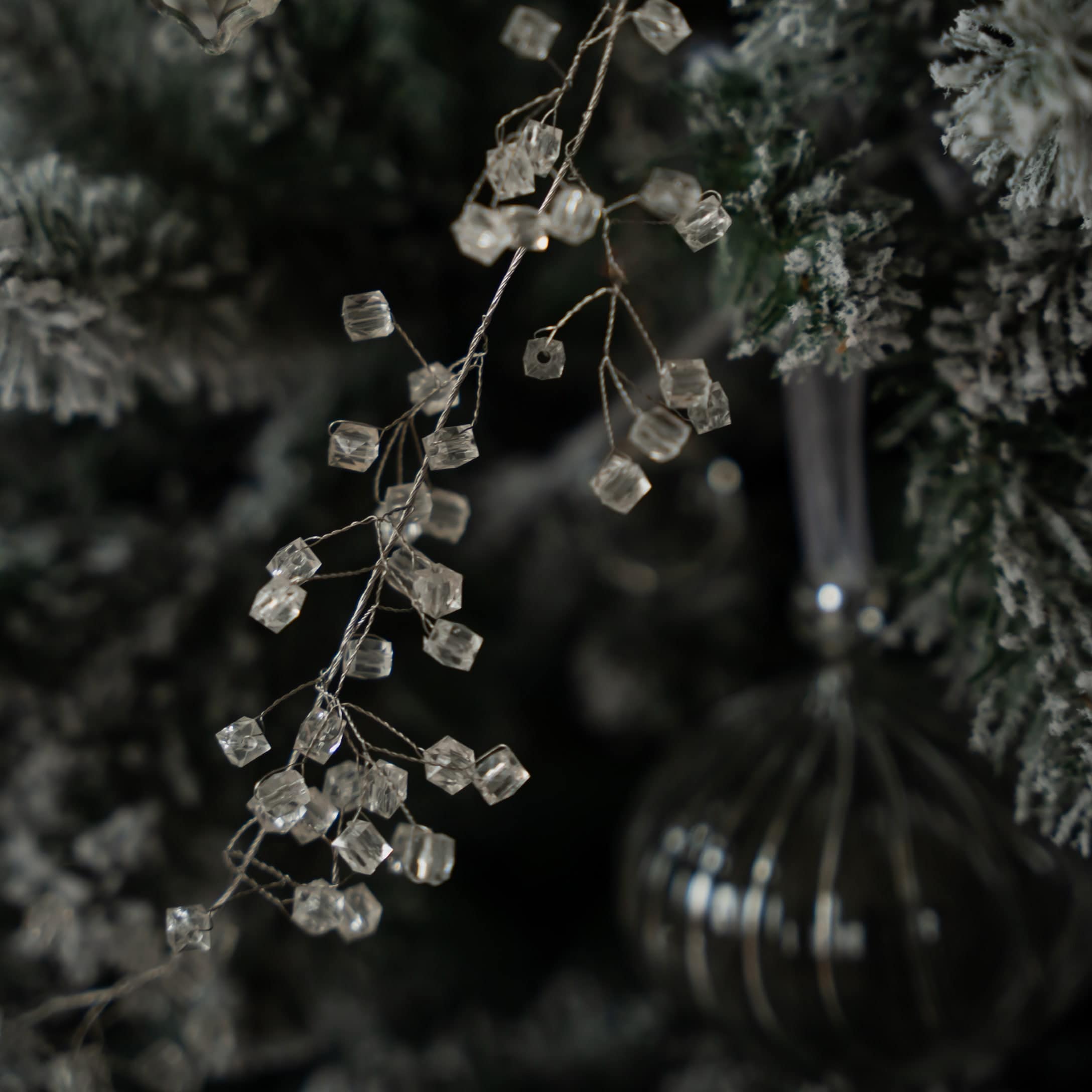Dekorative transparente Kristallperlen an Zweig vor künstlichem, schneebedecktem Weihnachtsbaum.