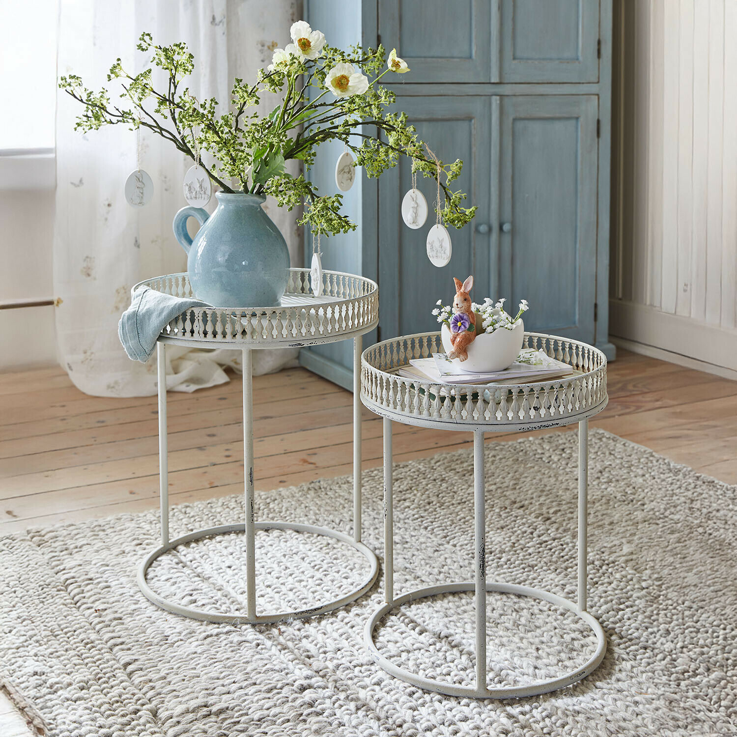 Beistelltisch 2er Set Vireline Zwei weisse Metall-Beistelltische mit filigranem Rand auf grauem Teppich, dekoriert mit Vase und Hasenfigur