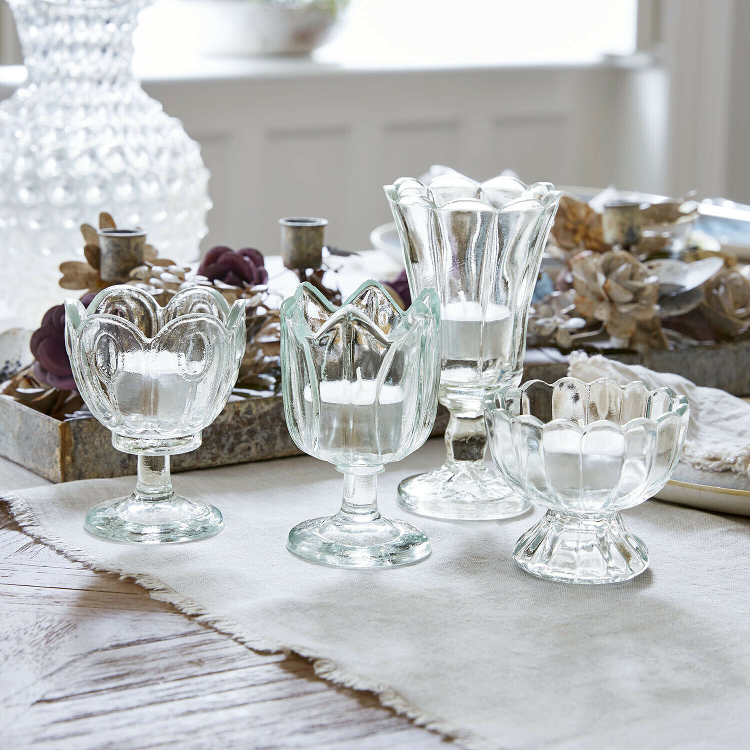 Windlicht 4er Set Amisette Set mit vier transparenten Glas-Teelichthaltern in verschiedenen Formen auf hellem Tuch