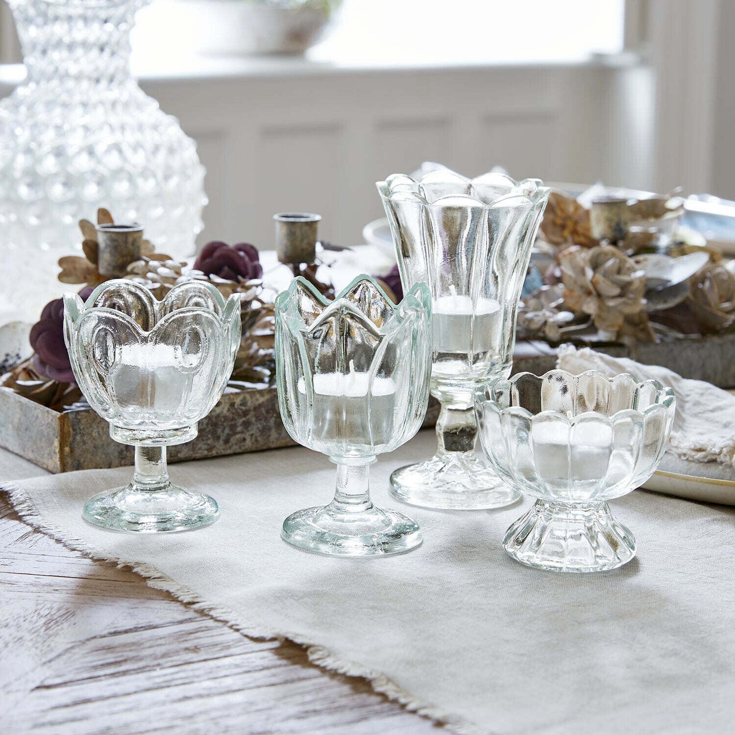 Windlicht 4er Set Amisette Set mit vier transparenten Glas-Teelichthaltern in verschiedenen Formen auf hellem Tuch
