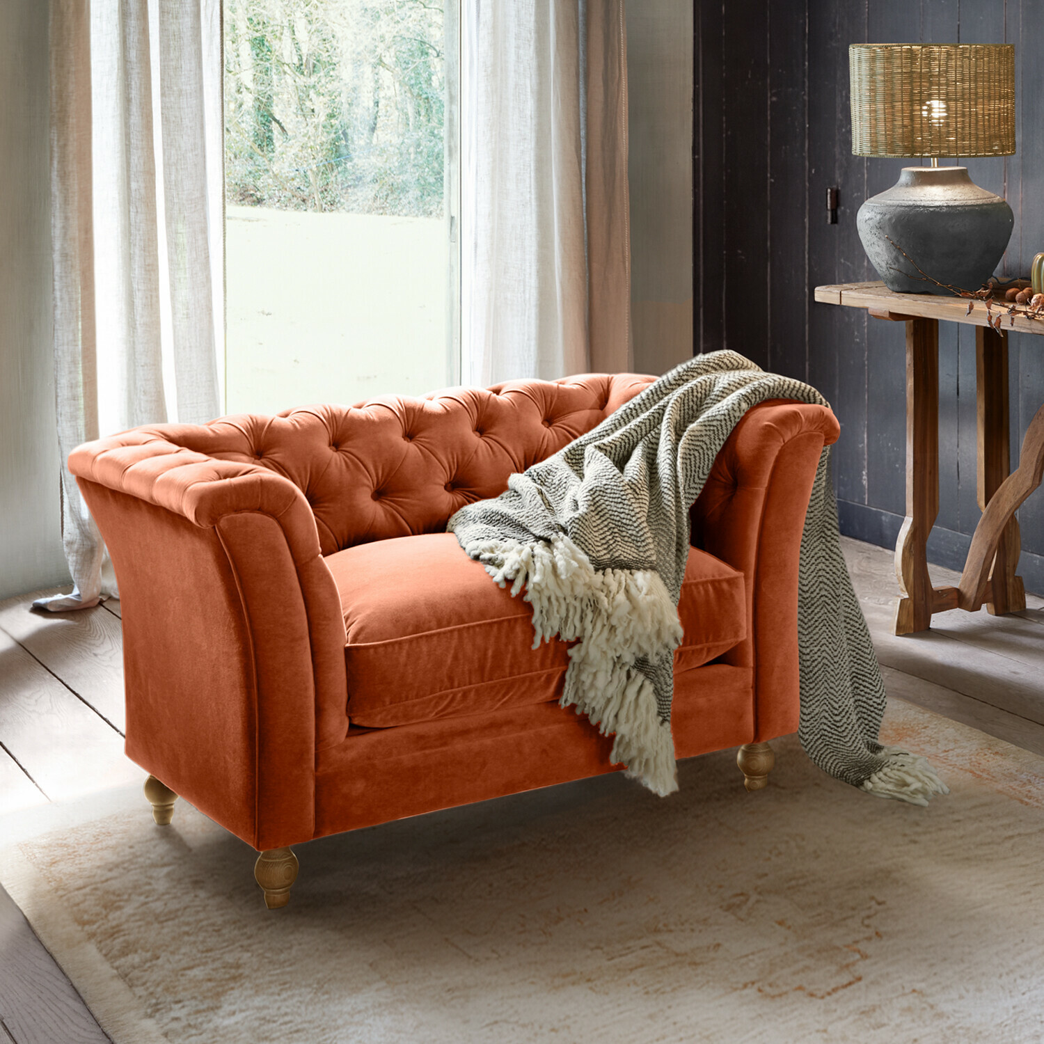 Oranges Samt-Chesterfield-Sofa mit grauem Plaid in gemütlichem Wohnzimmer mit Lampe und Holztisch