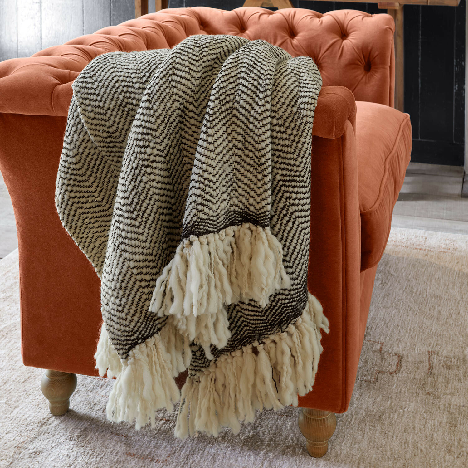Plaid Kerenza Weiche schwarz-weisse Kuscheldecke mit Fransen auf orangefarbenem Samtsofa im Wohnzimmer