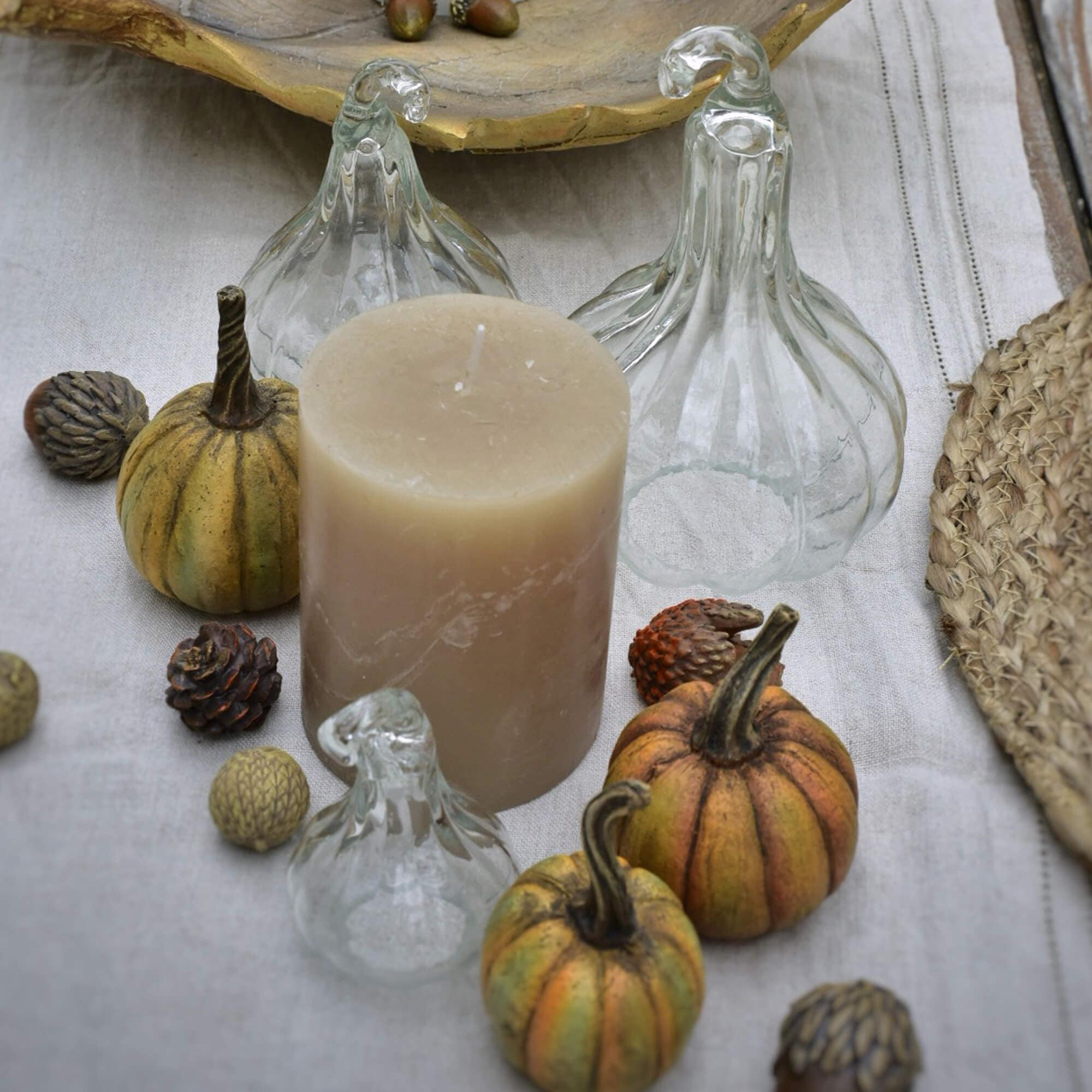 Beige Kerze mit dekorativen Glas-Kürbissen und kleinen Herbstdekorationen auf Leinentuch
