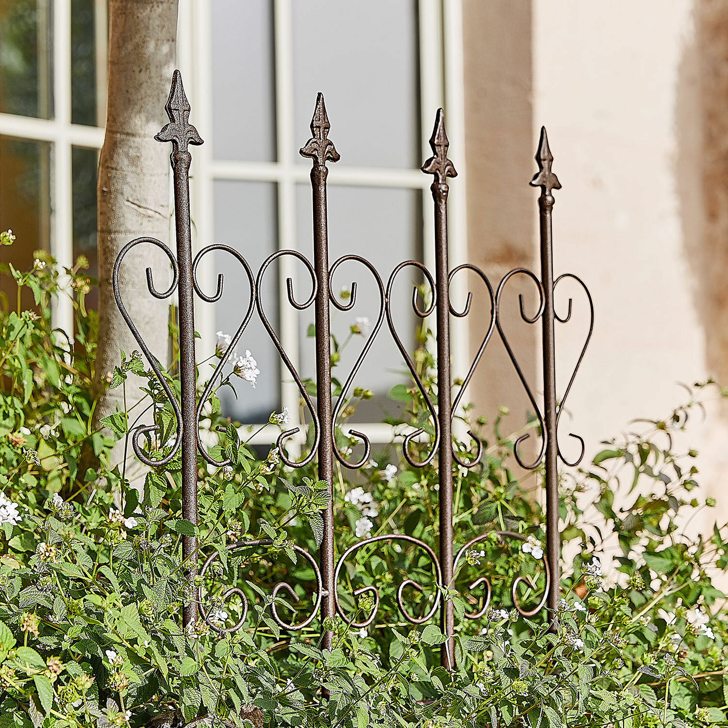 Rankhilfe Nectarise Dekorativer Gartenzaun aus rostbraunem Metall mit Herzmotiv, umgeben von grünen Pflanzen und weissen Blüten