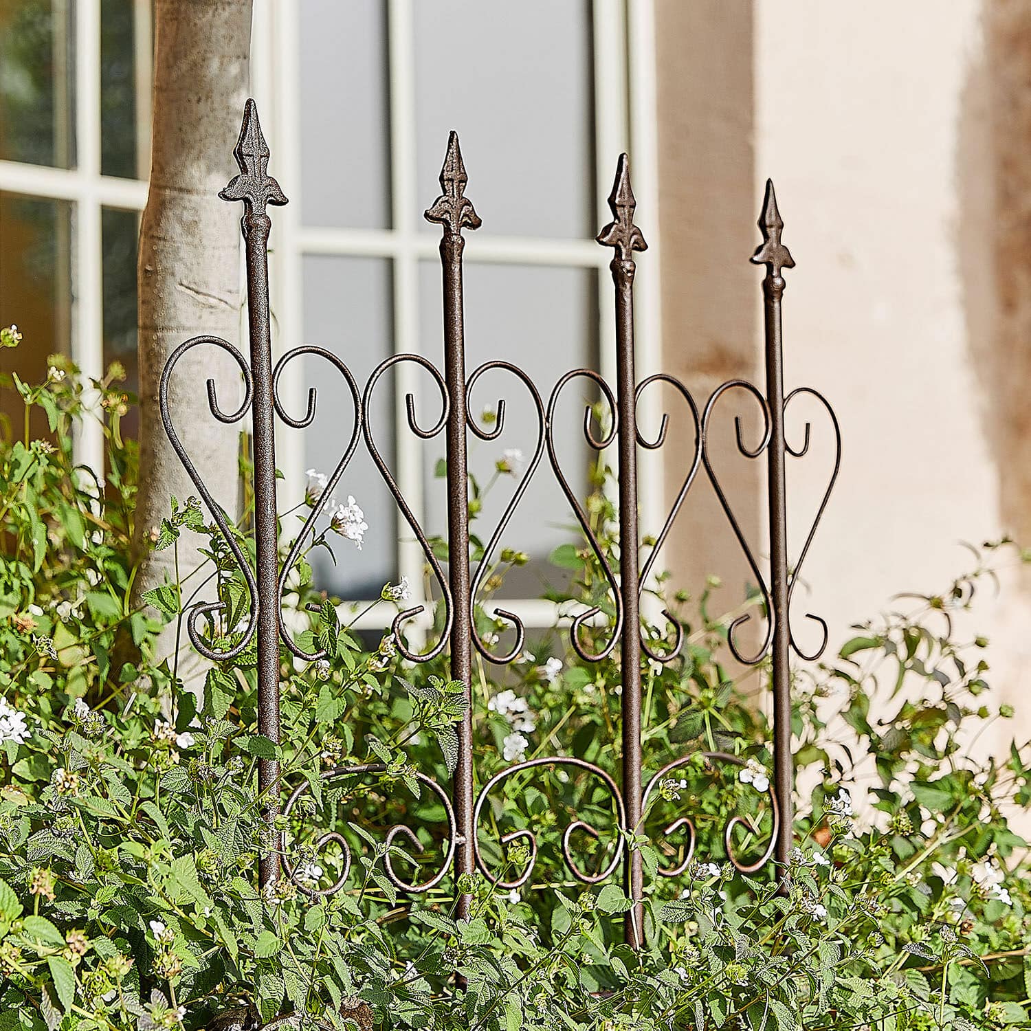 Rankhilfe Nectarise Dekorativer Gartenzaun aus rostbraunem Metall mit Herzmotiv, umgeben von grünen Pflanzen und weissen Blüten
