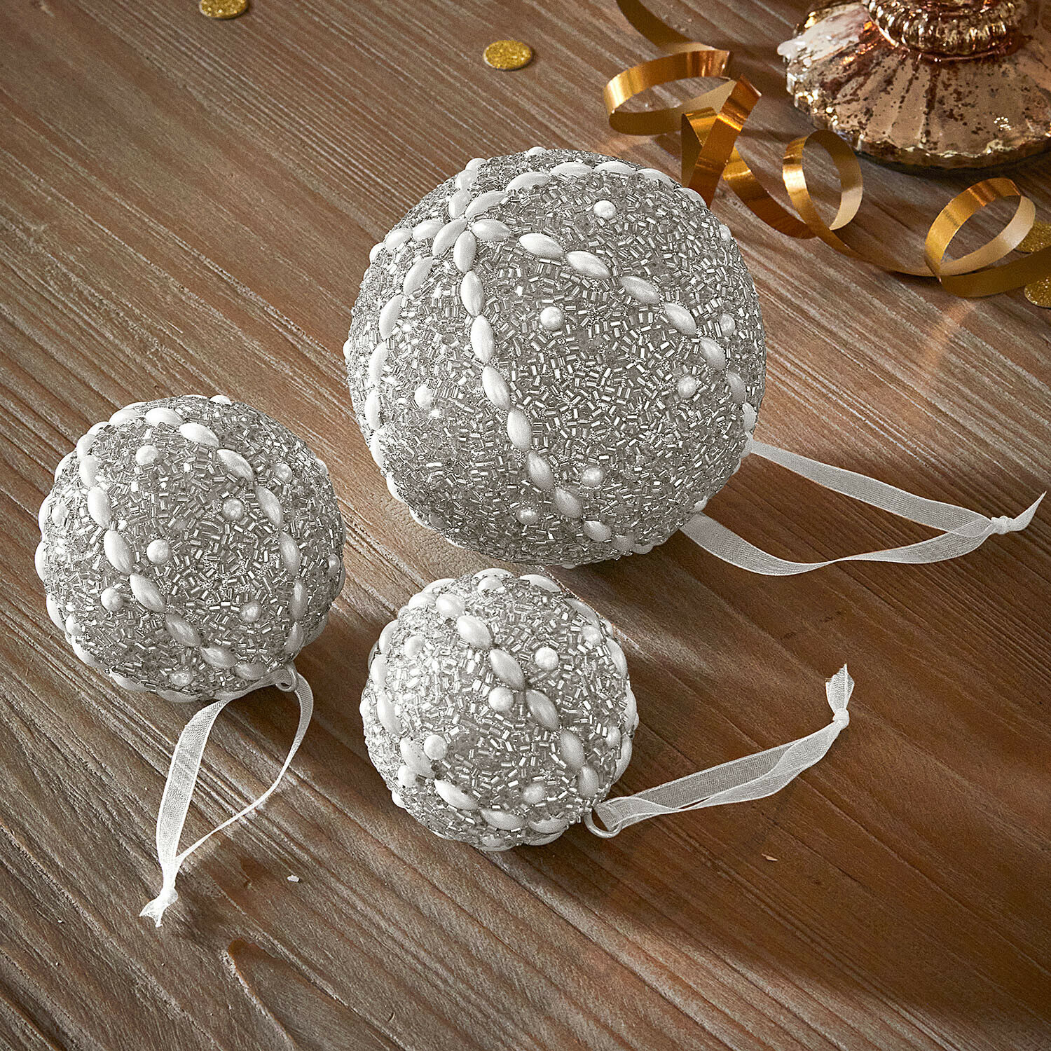Weihnachtskugel 3er Set Maelvik Set mit drei silbernen Weihnachtskugeln mit Perlen und Bändern auf Holztisch