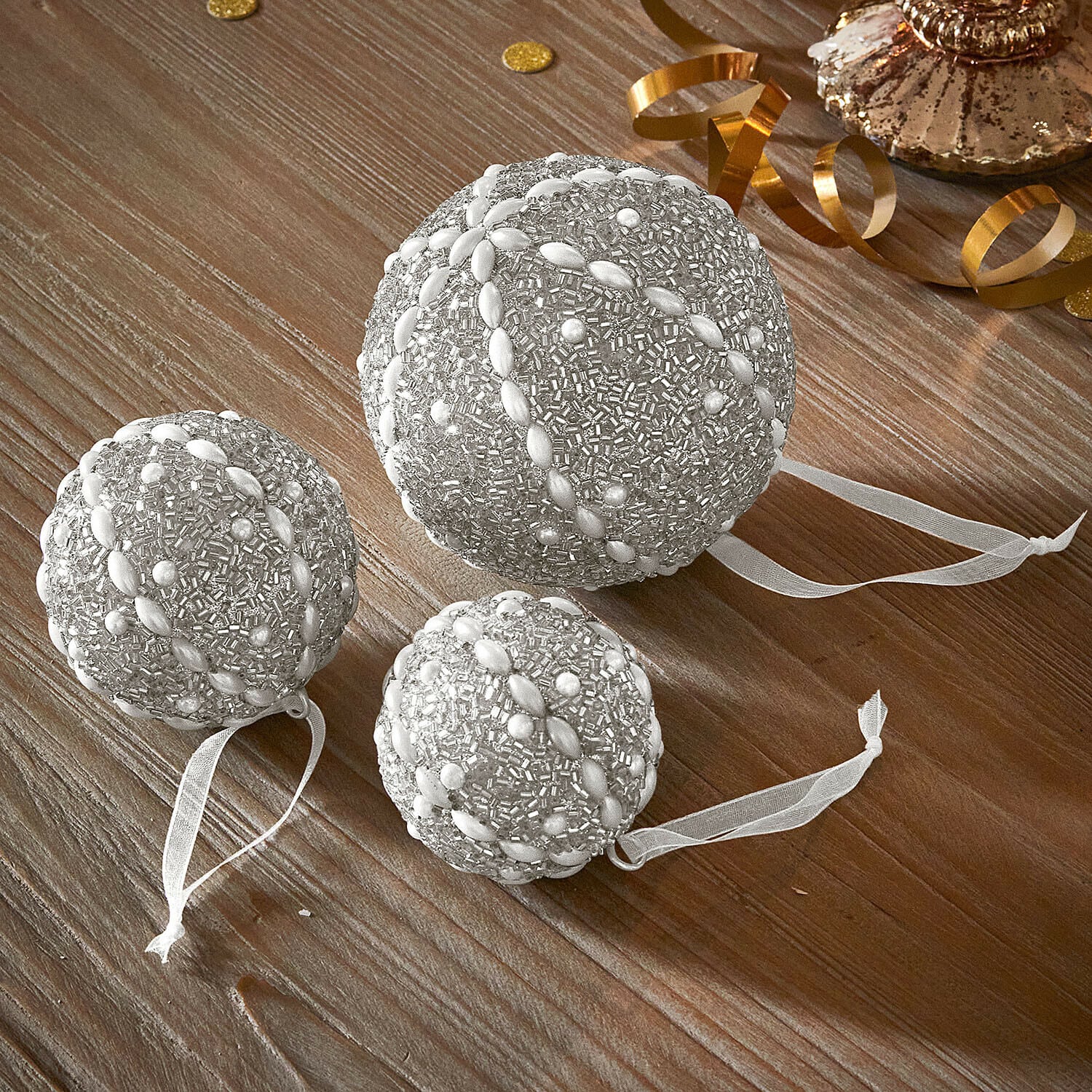 Weihnachtskugel 3er Set Maelvik Set mit drei silbernen Weihnachtskugeln mit Perlen und Bändern auf Holztisch