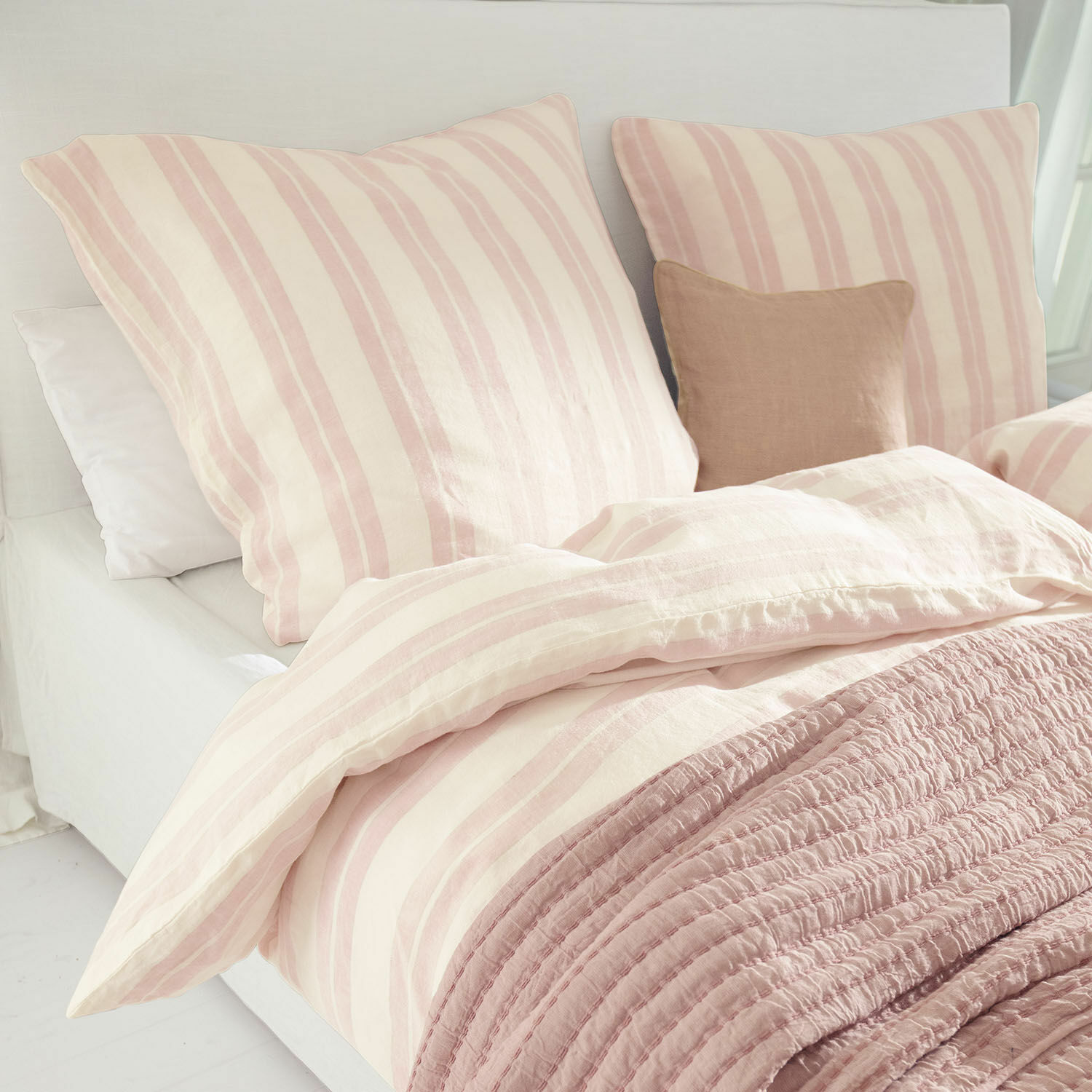 Bettwäsche Bettwäsche aus Baumwolle in rosa-cremefarbenen Streifen mit weicher rosa Decke auf hellem Bett.