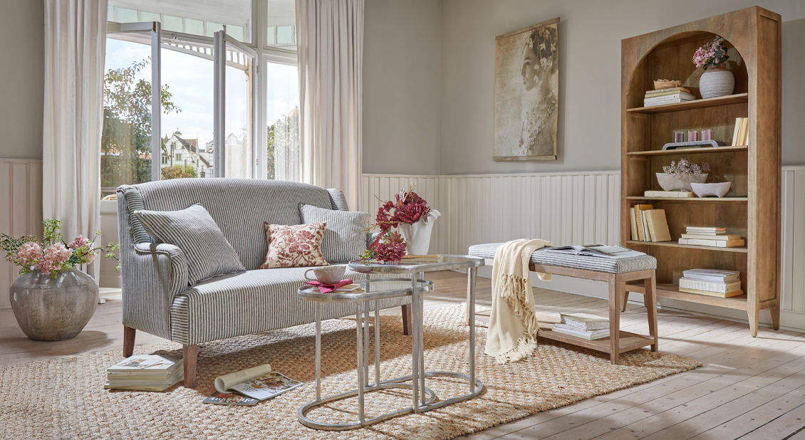 Gemütliches Wohnzimmer mit grauem, gestreiftem Sofa und Holzbänken auf Juteteppich, natürliche Möbel und Dekoration