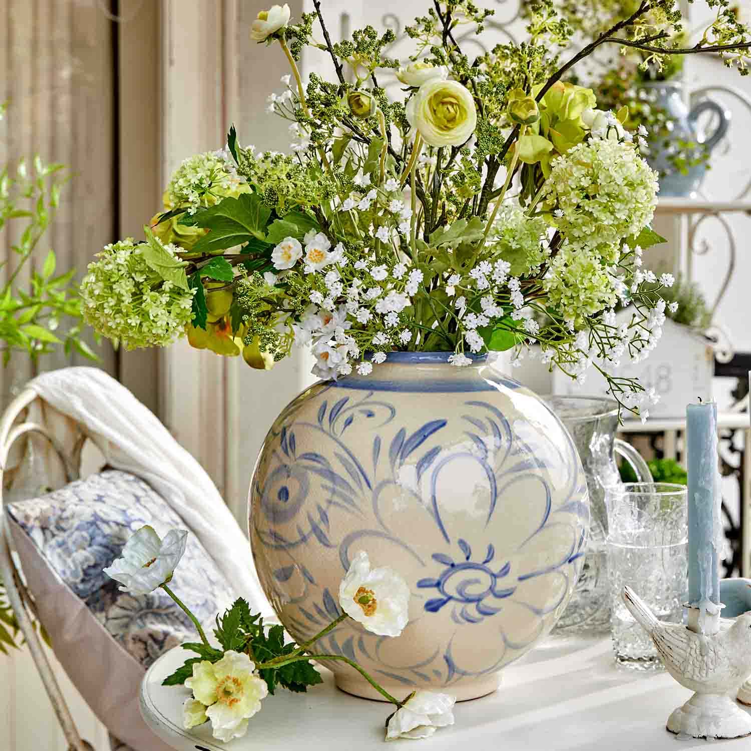 Runde Keramikvase mit blauem Blumenmuster und grün-weissen Blumen auf einem Tisch