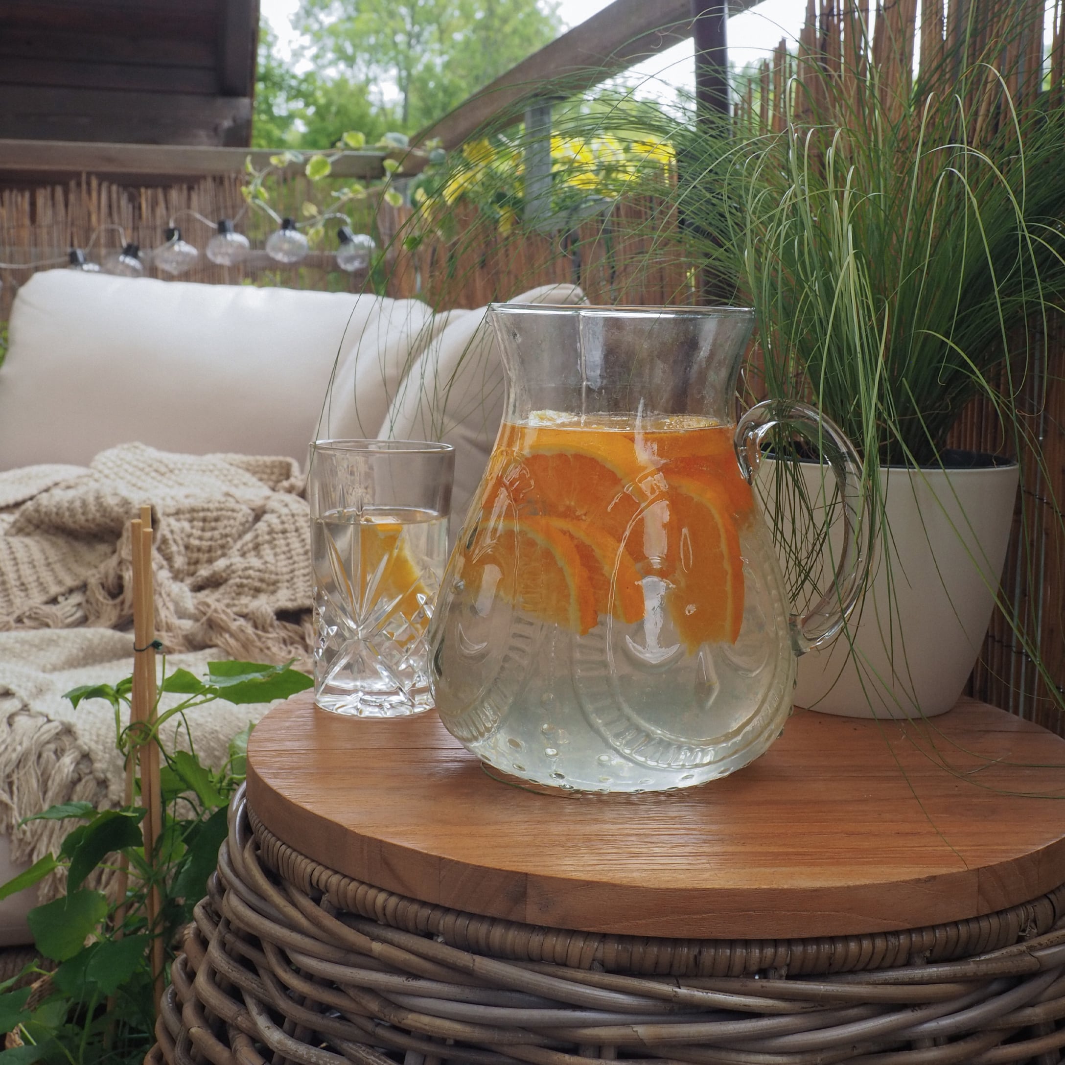 Glaskrug mit Wasser und Orangenscheiben auf Holztisch auf Terrasse mit Pflanzen