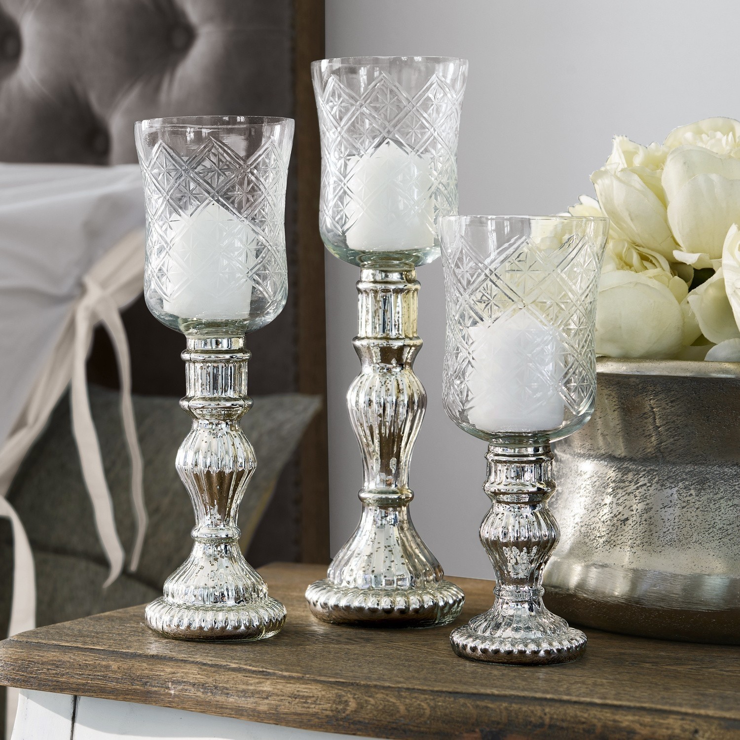 Windlicht 3er Set Celestin Drei silberne Kerzenhalter aus Glas mit Metallfuss dekorativ auf einem Holztisch arrangiert