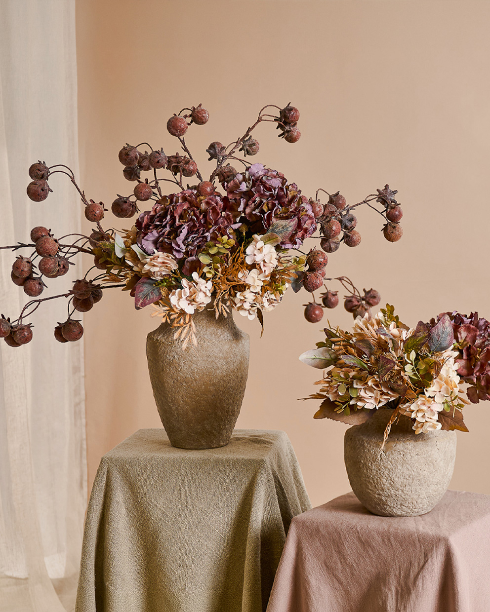 Zwei dekorative beige Steinvase mit herbstlichen Blumen und getrockneten Früchten auf Tischen