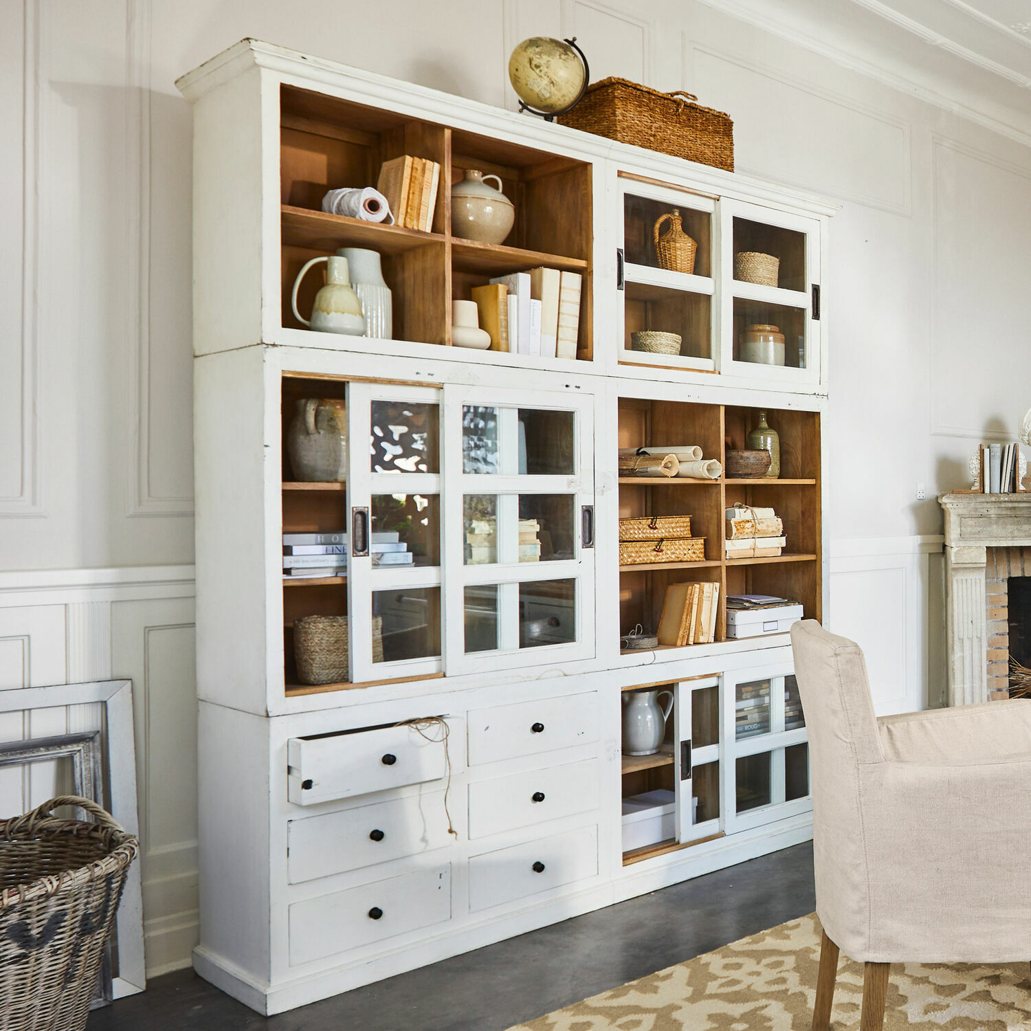 Schrank Dubberly Weisser Holzschrank mit Glastüren und Schubladen im Vintage-Stil, dekoriert mit Büchern und Körben