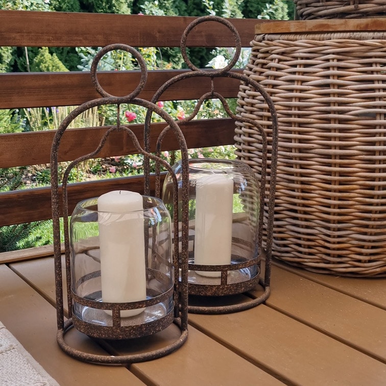 Zwei dekorative Laternen mit Metallrahmen und weissen Kerzen auf einem Holztisch im Garten