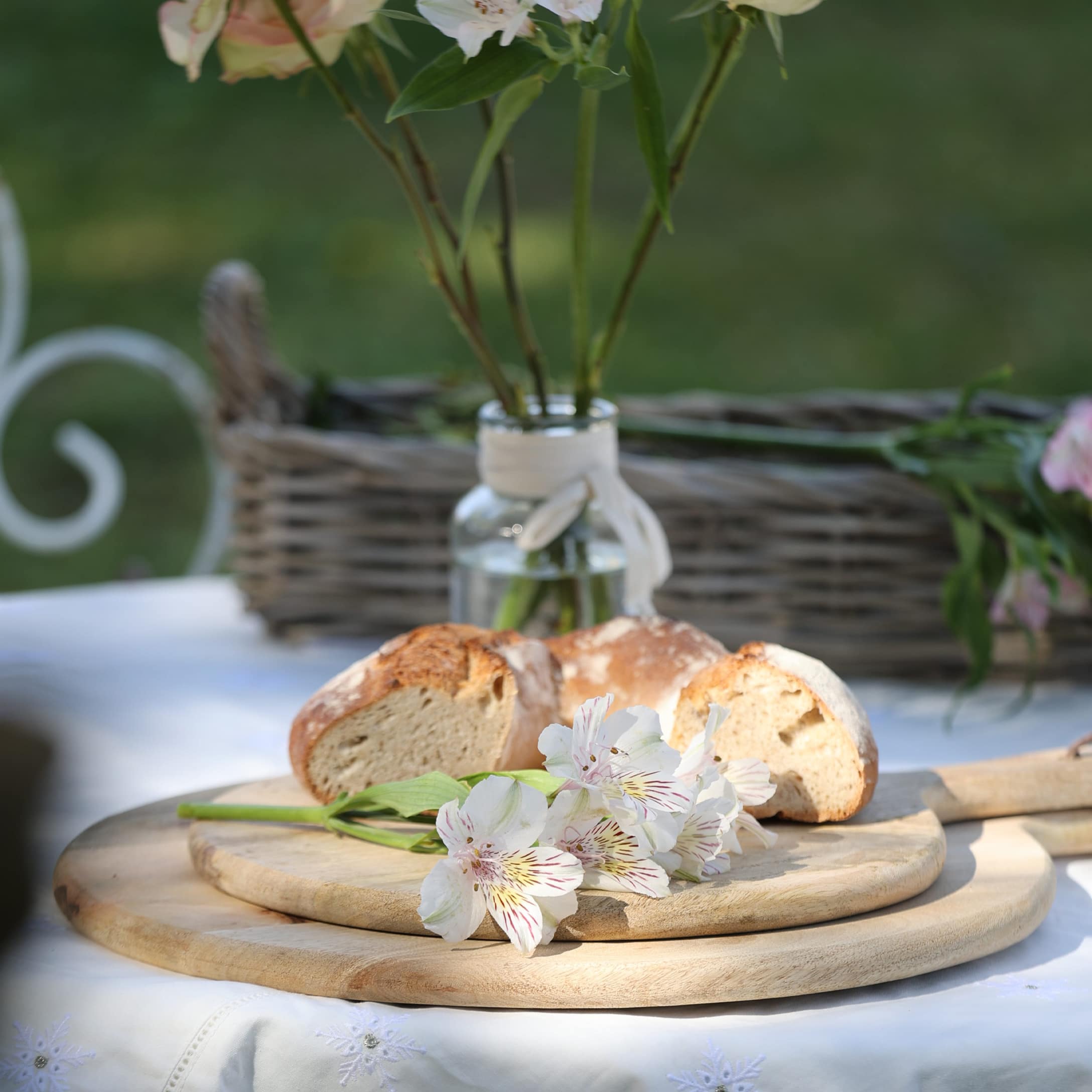 Holzschneidebrett mit weissen Blumen und Brot auf weiss gedecktem Tisch im Garten