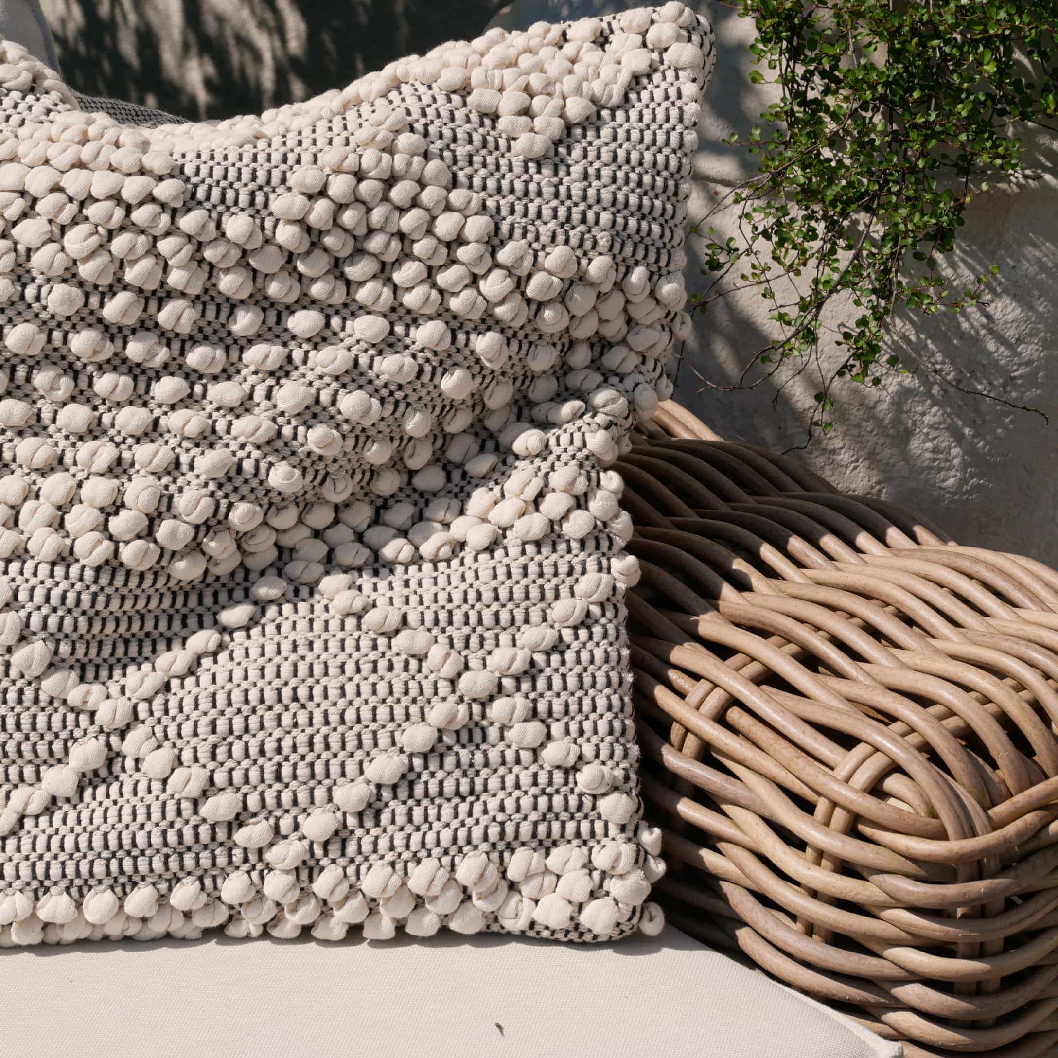 Dekoratives Baumwollkissen in Creme-Grau auf einem Rattansessel im Boho-Stil