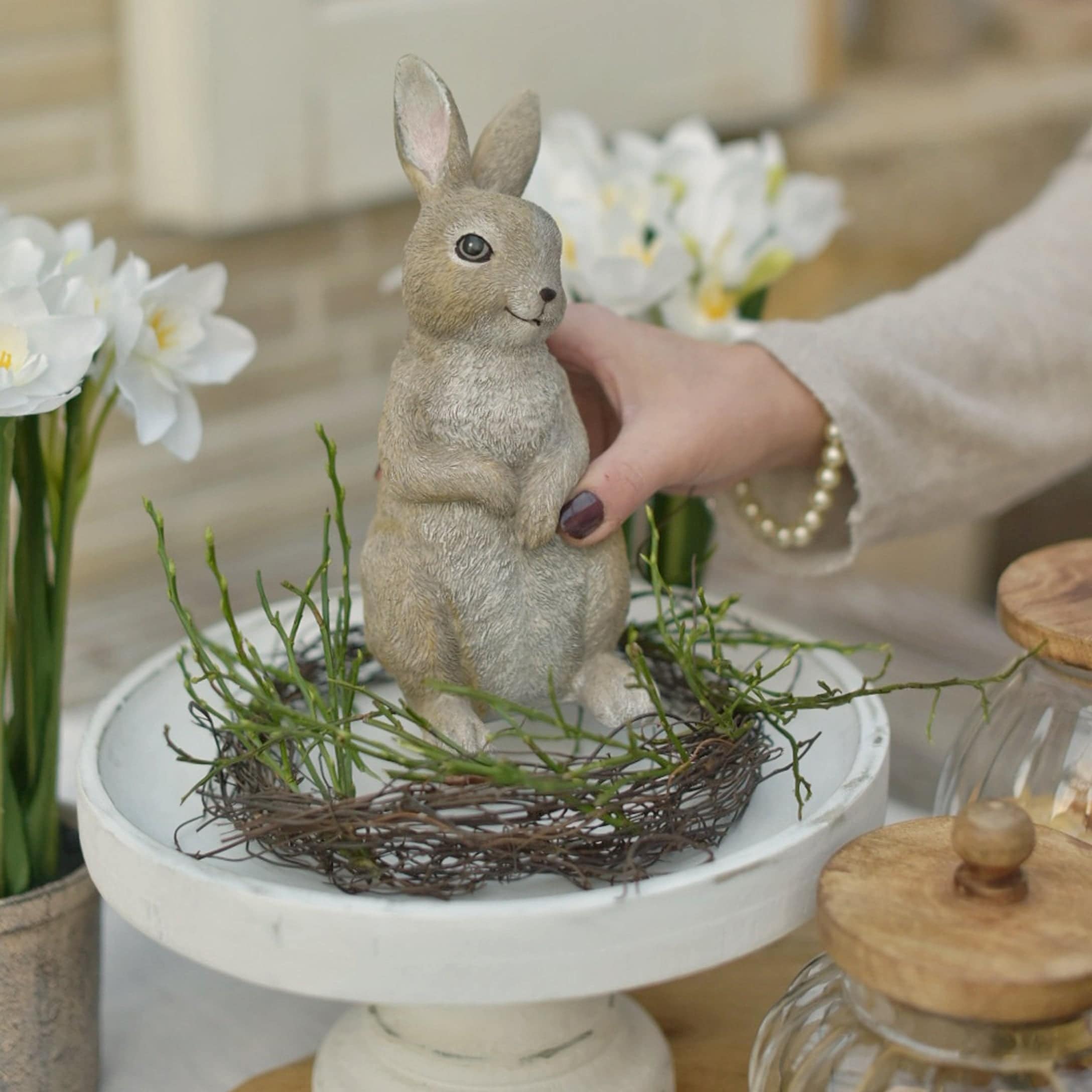 Dekorativer Osterhase in natürlichen Farben auf weissem Podest mit grünen Zweigen