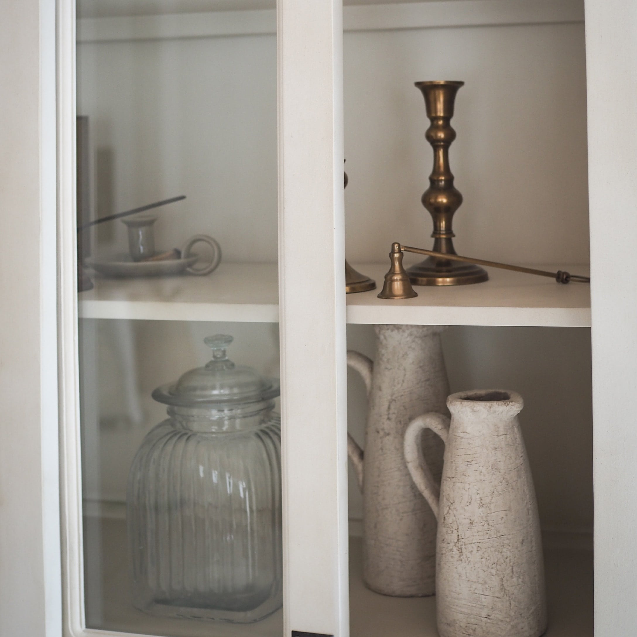 Glasbehälter und weisse Keramikkrüge im weissen Schrank mit Messingkerzenhalter und Glocke