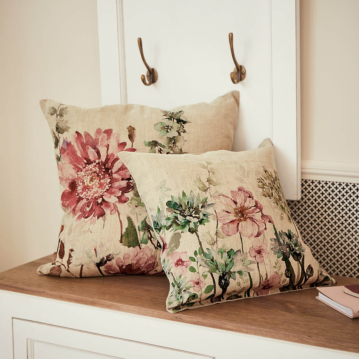Zwei Leinenkissen mit pastellfarbenem Blumenmuster auf hellem Holz als dekorative Wohnaccessoires