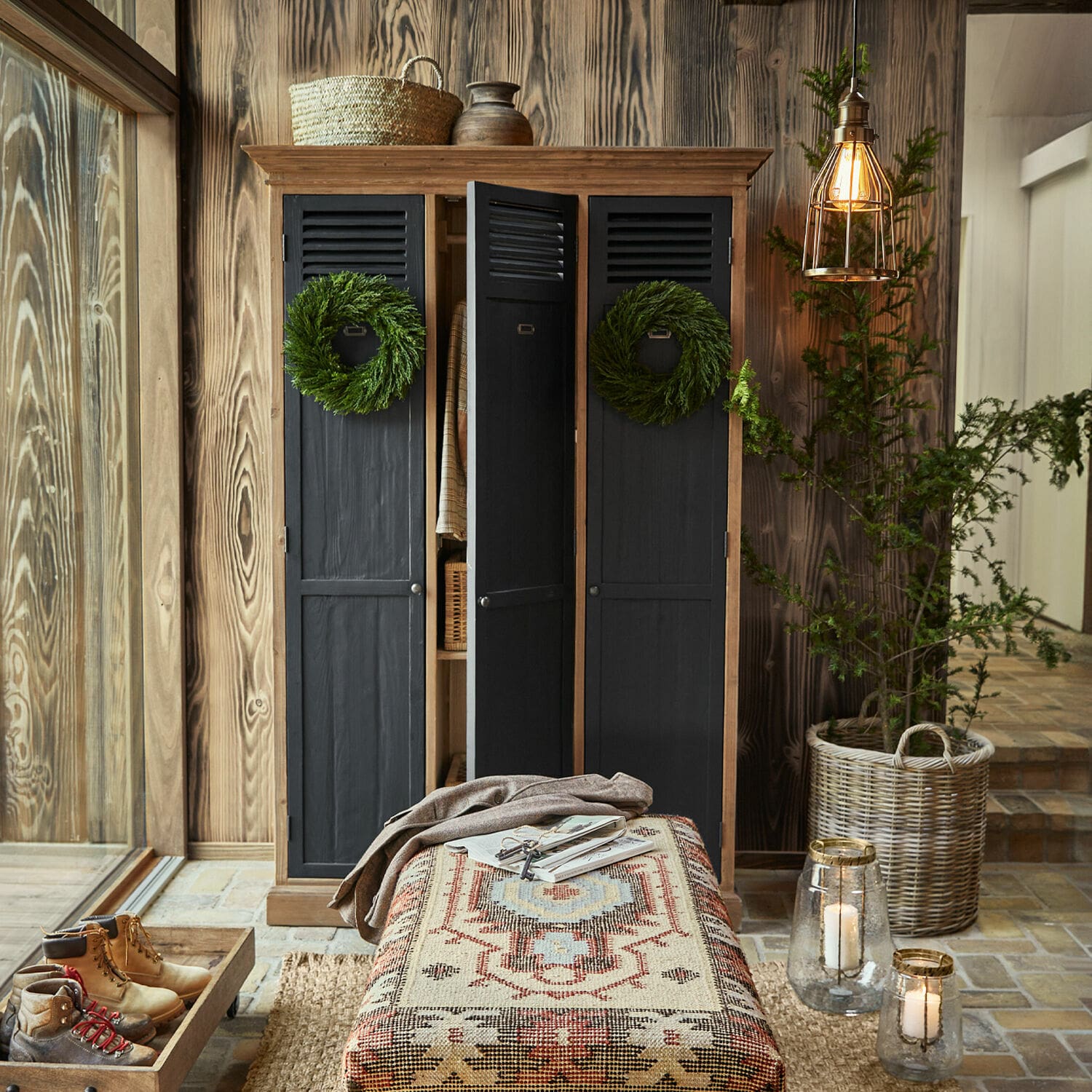 Schrank Hillcroft Dreiteiliger schwarzer Holzschrank mit grünen Kränzen und gemusterter Hocker in gemütlichem Naturmaterial-Interieur