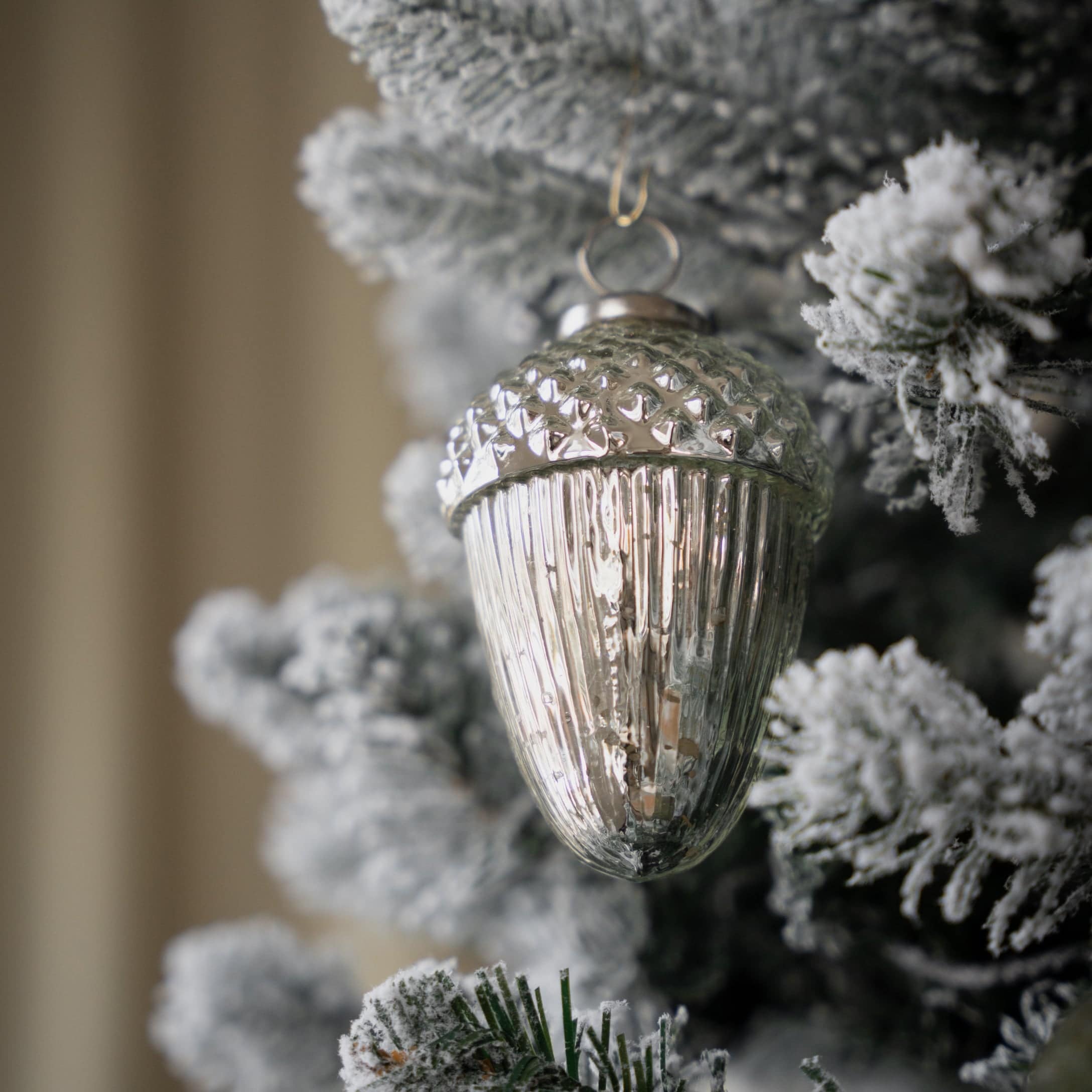 Silberne Glas-Weihnachtsbaumkugel in Eichelform an schneebedecktem Tannenbaum