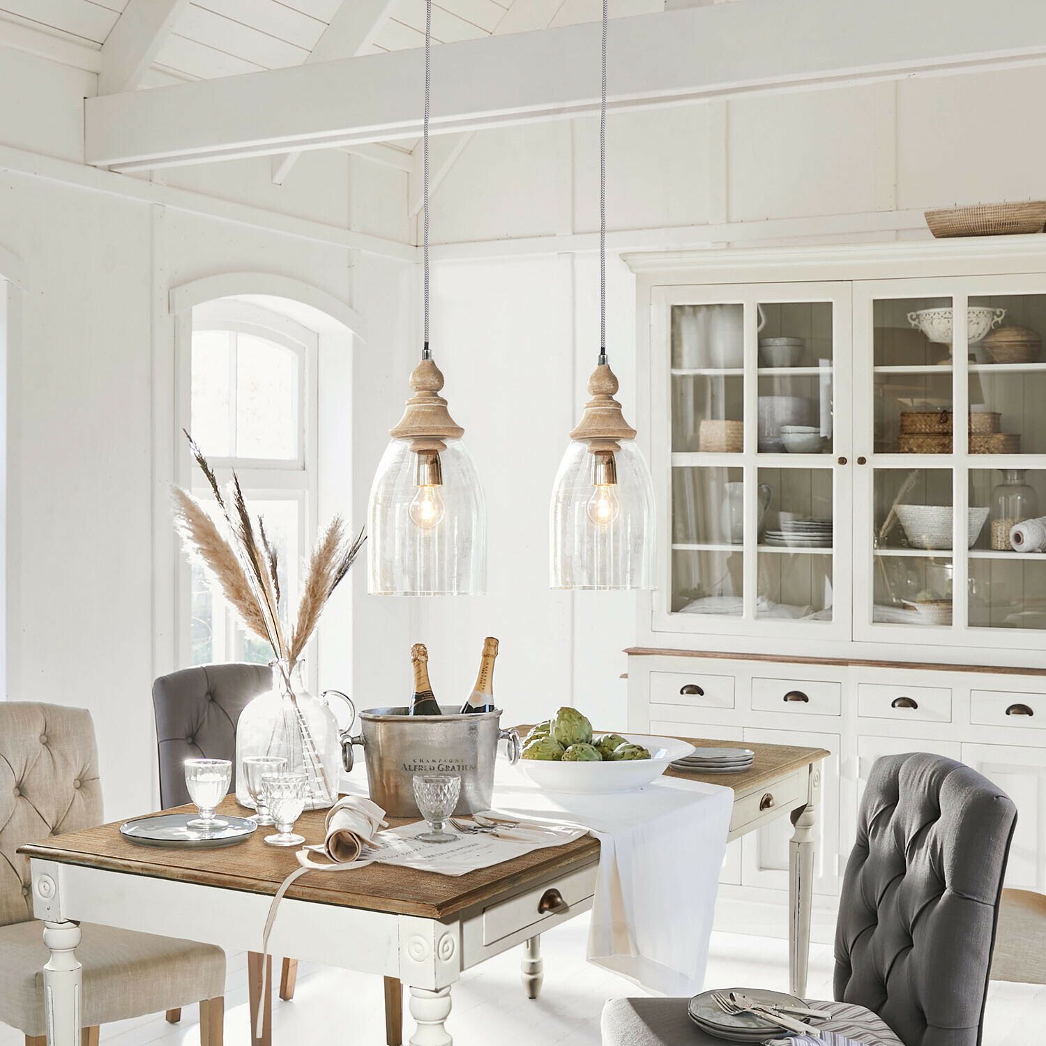Rustikaler Essbereich mit weissem Holztisch, grauen Polsterstühlen und Vitrinenschrank mit Korbdeko