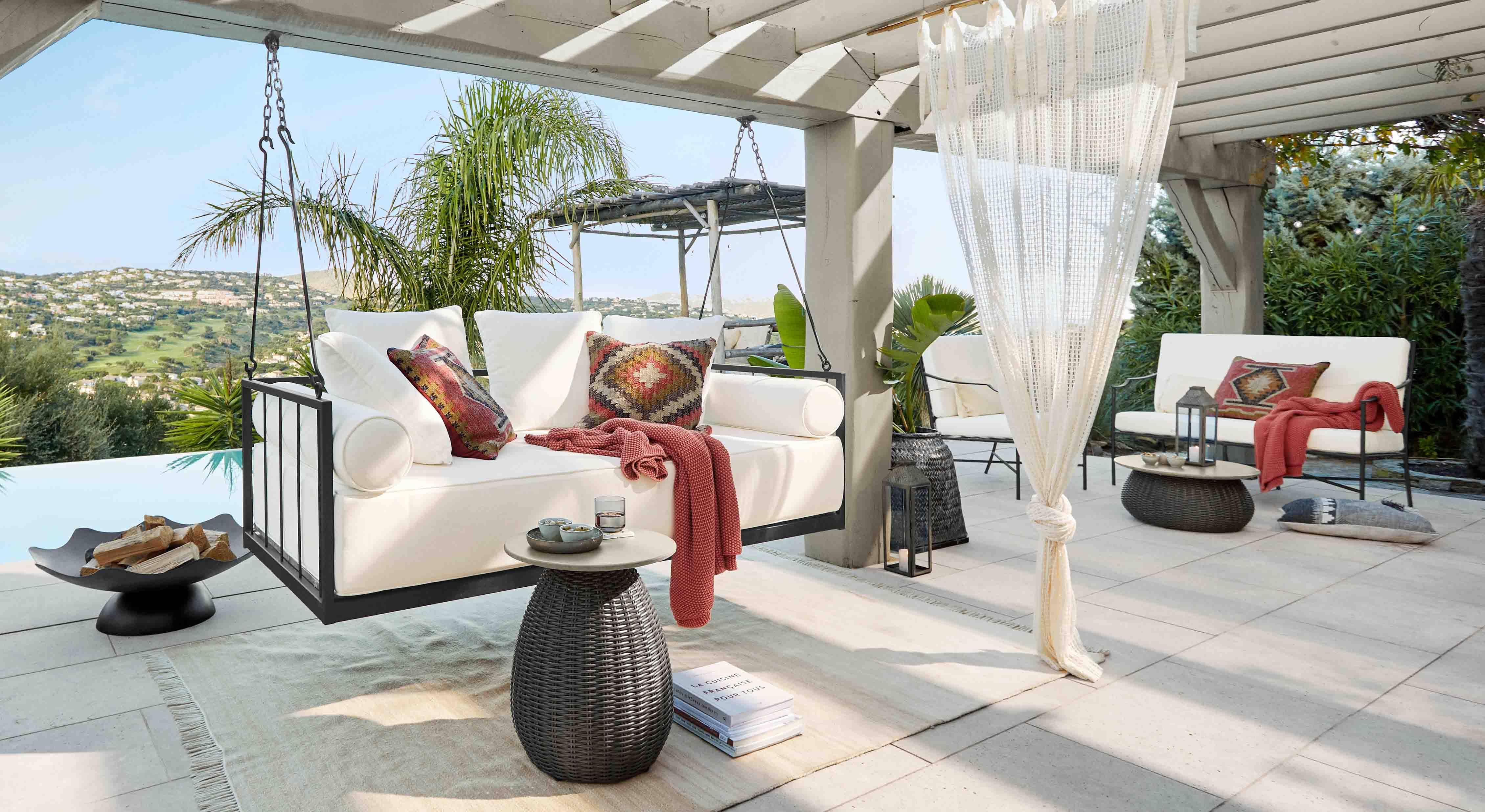 Weisse Hängesofa mit Metallrahmen und bunten Kissen auf Terrasse mit Hügelblick