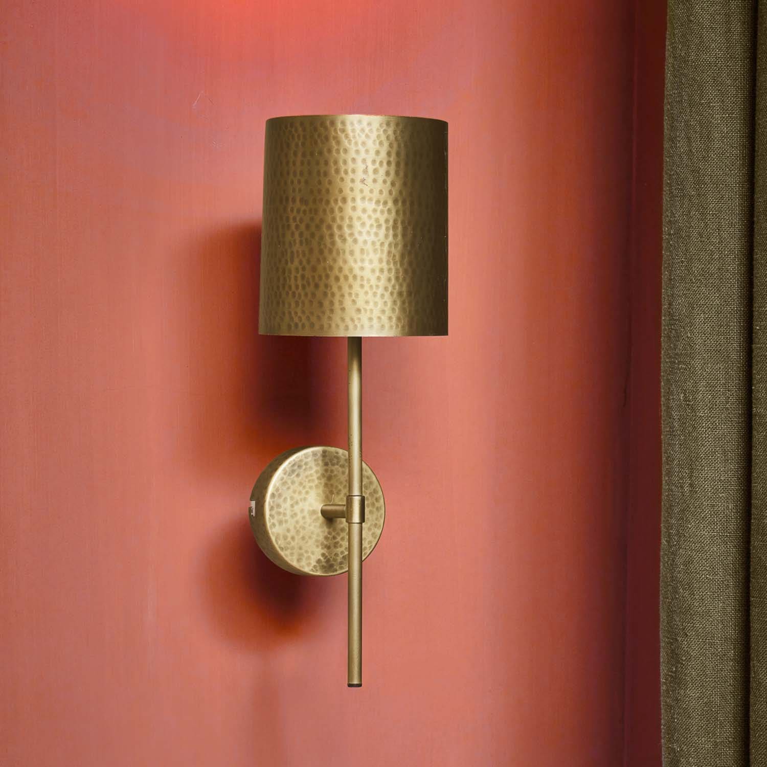 Wandleuchte aus gehämmertem Messing mit zylindrischem Schirm an roter Wand, dekorative Beleuchtung