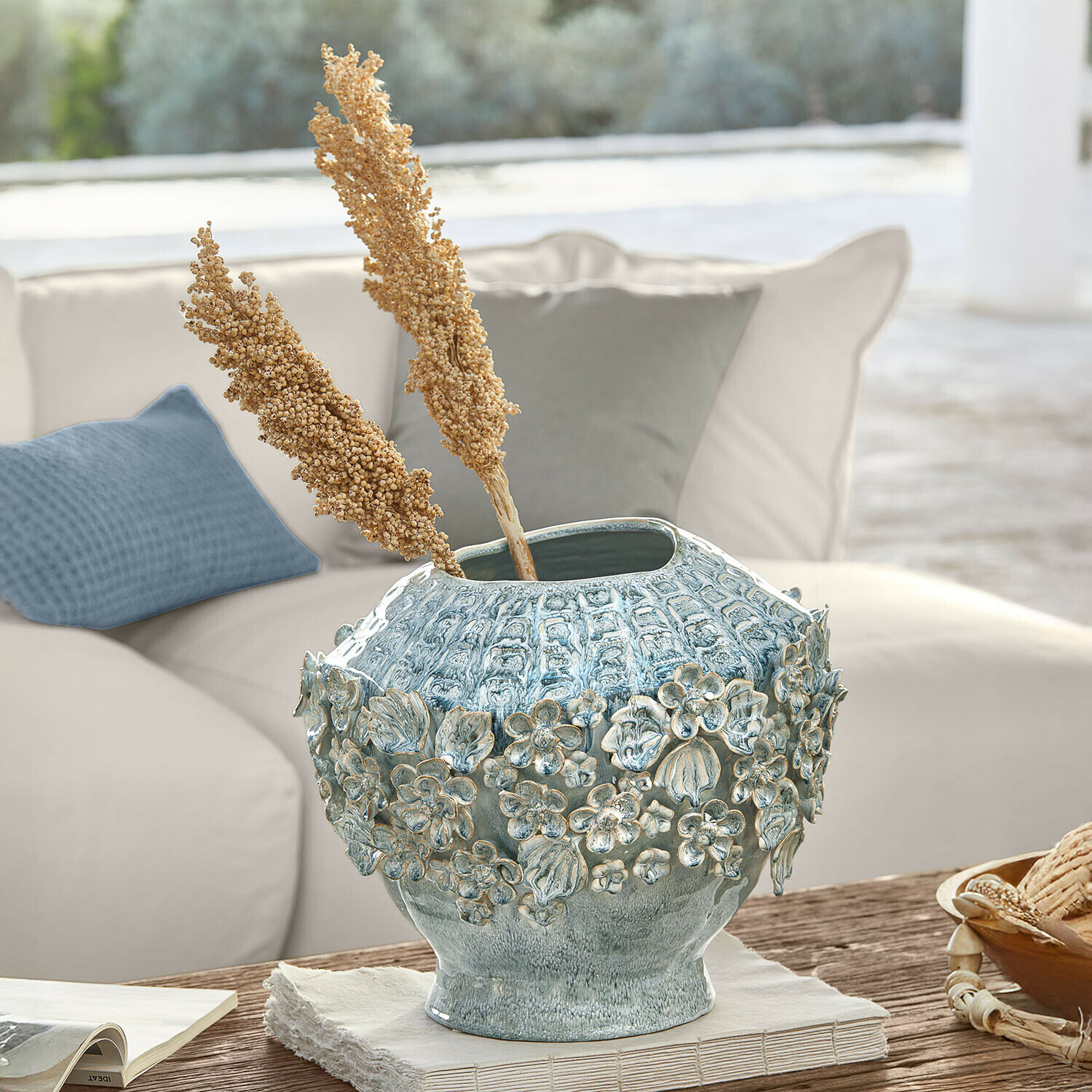 Dekorativer blauer Keramikvase mit Blumenrelief auf Holztisch im hellen Wohnzimmer