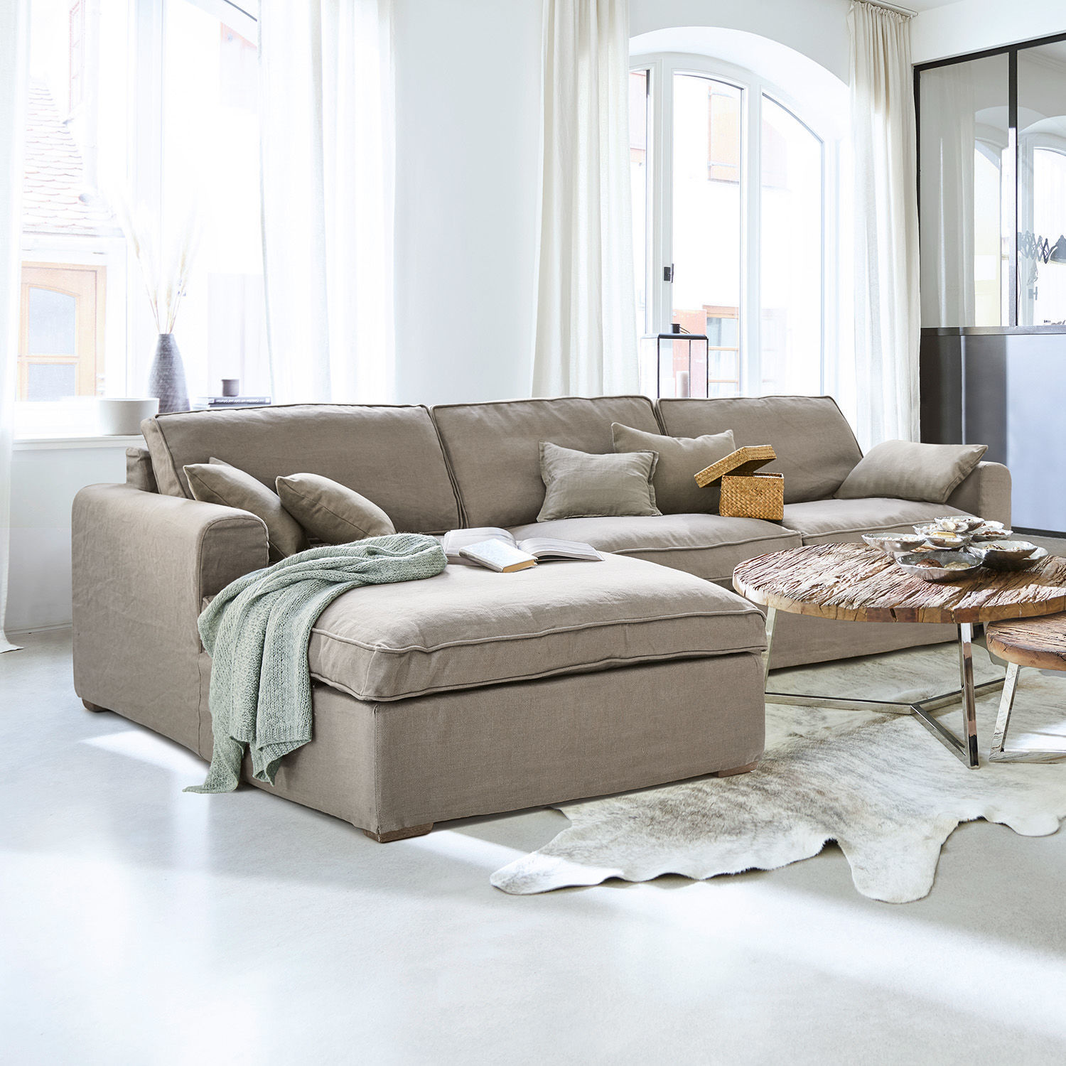 Sofa Seaford Beiges Ecksofa aus Stoff im hellen Wohnzimmer mit Holztisch und Dekorationen