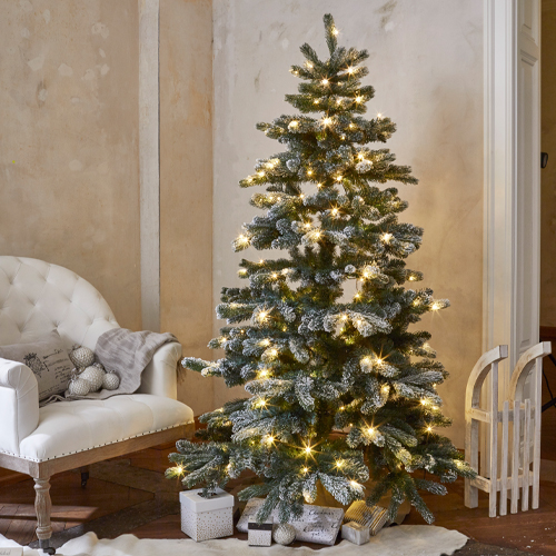 Künstlicher Weihnachtsbaum mit schneebedeckten Zweigen und warmen Lichtern als festliche Dekoration