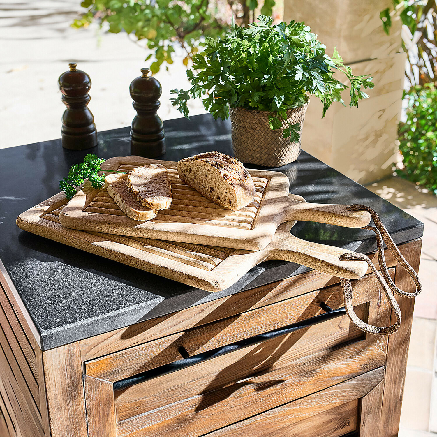 Drei Holz-Schneidebretter mit Griffen und Schlaufen, darauf Brot und frische Kräuter auf Küchenarbeitsplatte