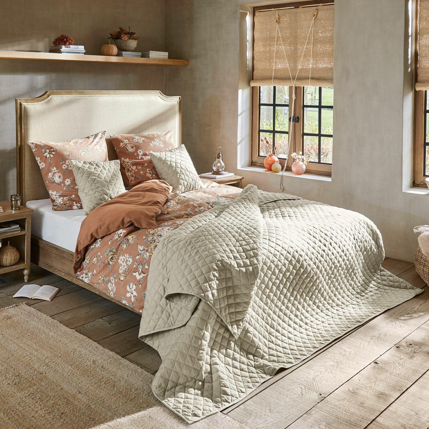 Bett Catham Gemütliches Schlafzimmer mit Bett in beiger Steppdecke und floraler Bettwäsche in warmen Farben.