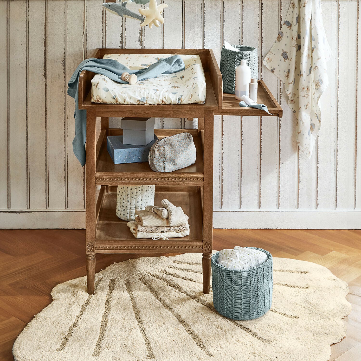 Teppich Vellaro Holzwickeltisch mit weicher Matte und blauem Windelkorb im Kinderzimmer